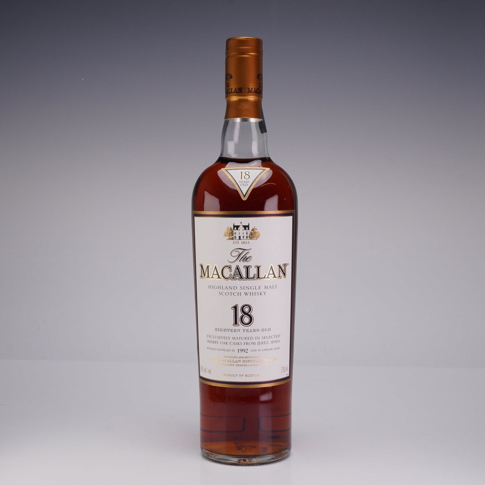 The Macallan Highland Single Malt Scotch Whisky 18 Years Old Distilled 1992: This lot features a 750ml bottle of The Macallan 18 Years Old Highland Single Malt Scotch Whisky, accompanied by its original purple geometric-patterned presentation box. The labels identify the whisk