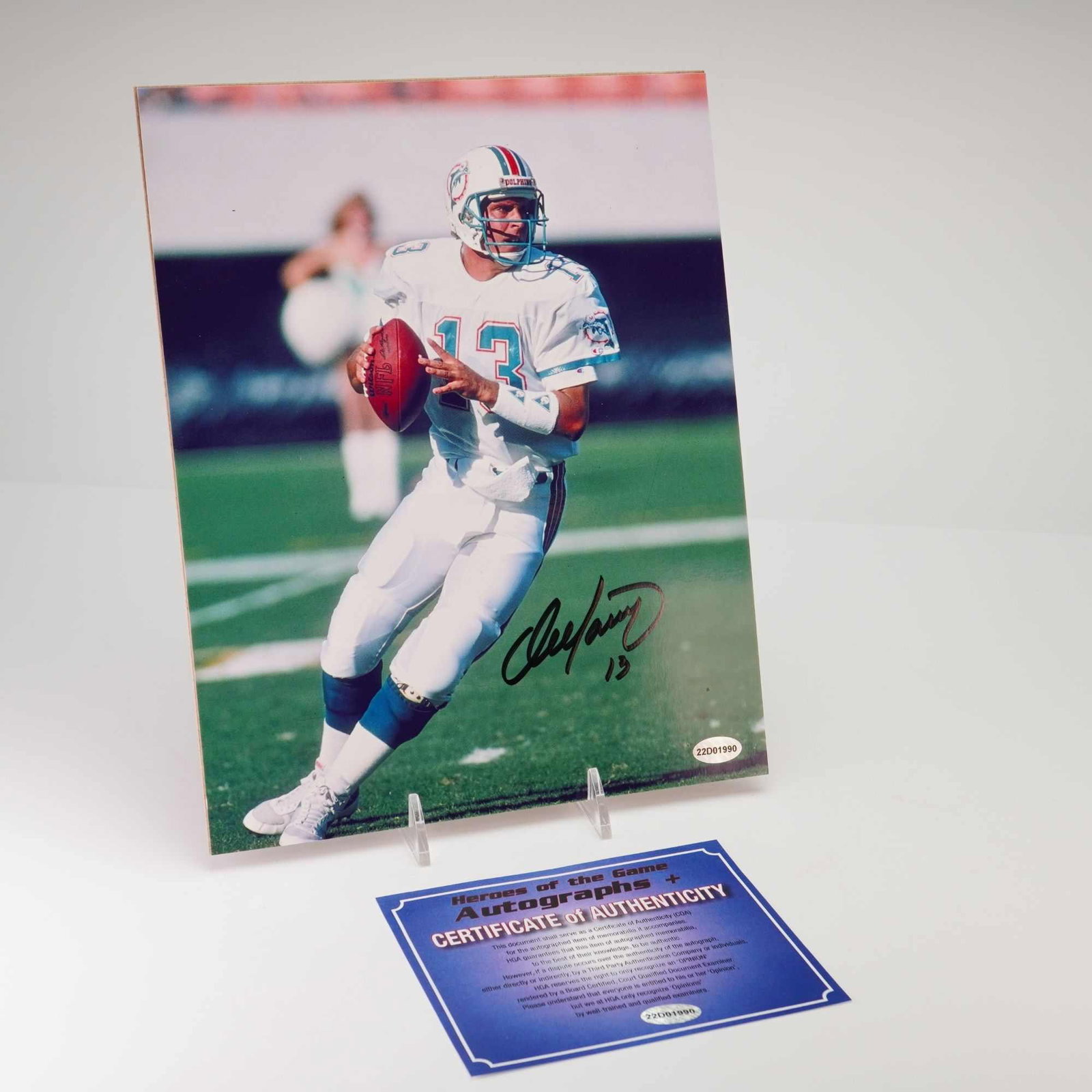 Dan Marino Signed Miami Dolphins Action 8x10 Photo with HGA COA: This lot features an autographed color photograph of Hall of Fame quarterback Dan Marino. The image depicts Marino in a white Miami Dolphins home jersey and helmet, captured in an on-field action pose