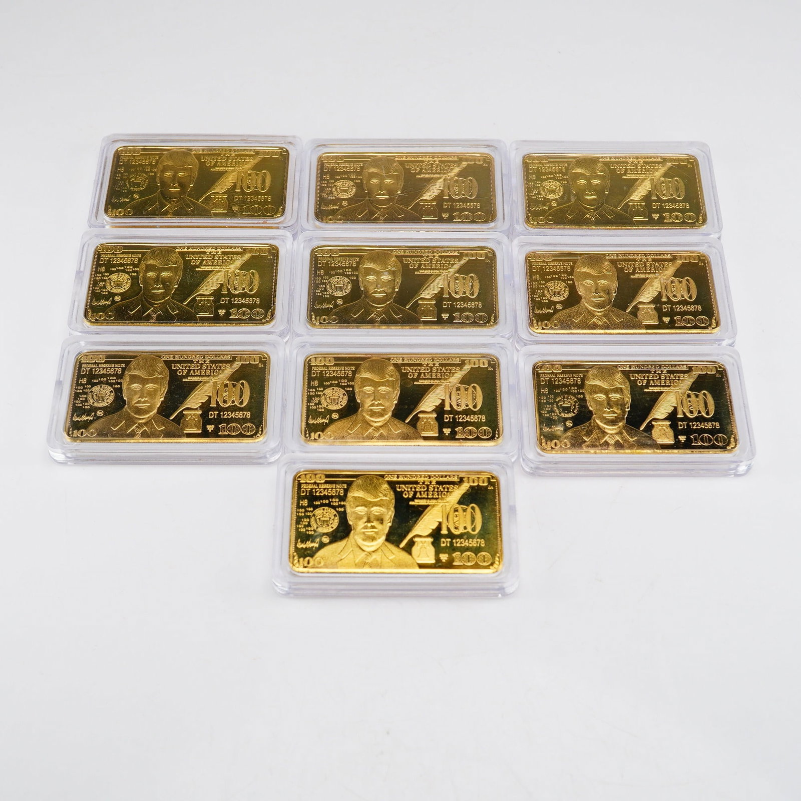 10 Berkley Jensen 100 Unit Commemorative Gold-Plated Donald Trump Bars: A set of ten commemorative novelty gold-plated bars produced by Berkley Jensen, modeled after the design of a United States one hundred dollar bill. Each bar features an obverse portrait of Donald Tru