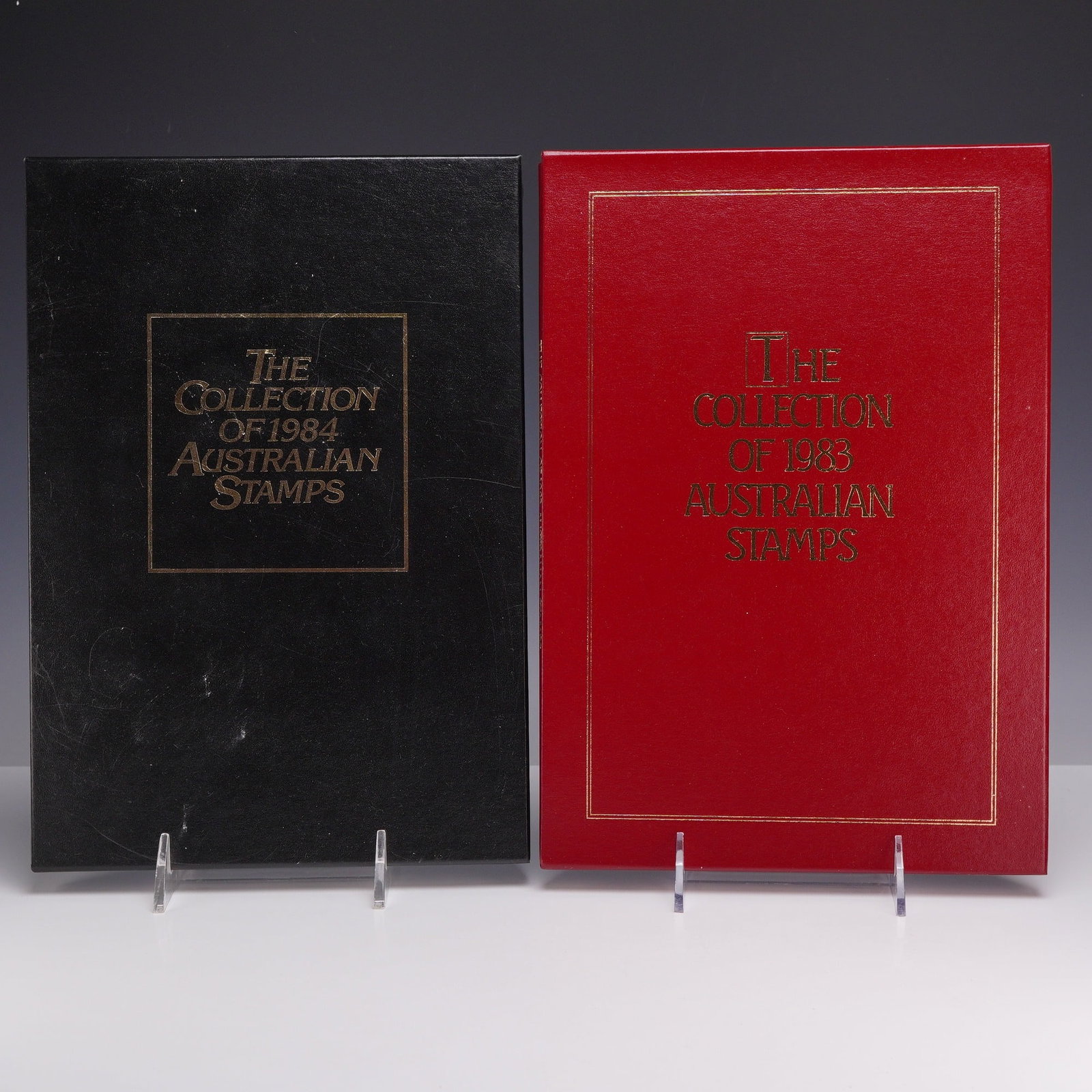 Two Sets AU 1983 & 1984 Annual Collection of Australian Stamps: This lot consists of two Australia Post annual stamp collection yearbooks. The first is titled The Collection of 1983 Australian Stamps, presented in a red textured hardcover, and the second is titled