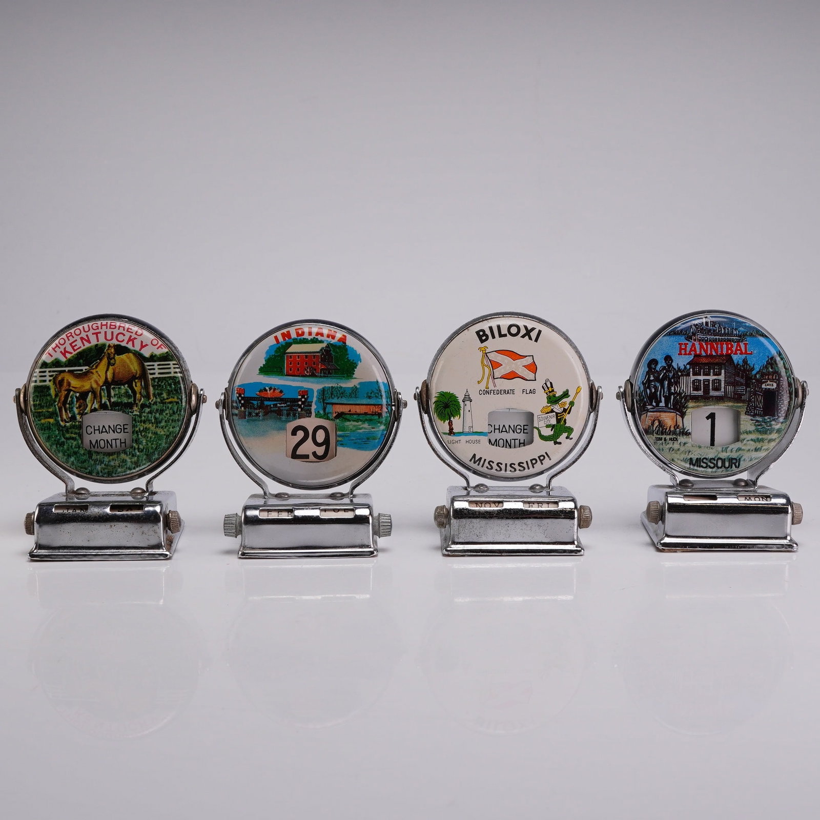 A Group of Four Vintage Chrome Mechanical Roll Top Perpetual Desk Calendars: This group of four mid-century mechanical roll top perpetual desk calendars are constructed with a chrome-plated metal frame and a rectangular base. The calendars feature a circular swiveling face tha