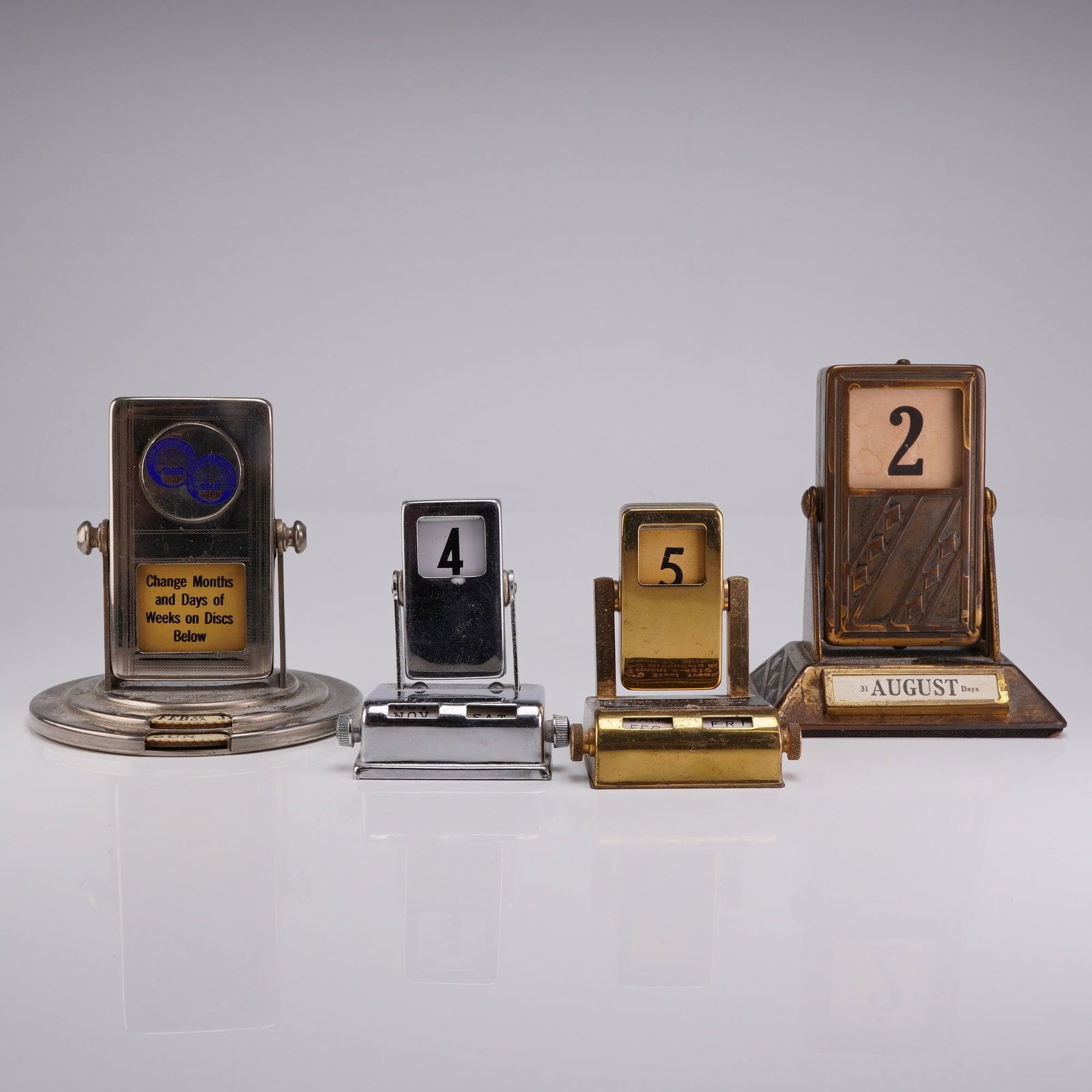 Collection of Four Vintage Roll Top Perpetual Desk Calendars: This 4 roll top calendar collection includes four vintage perpetual desk calendars of various styles and materials dating from the late 1920s through the mid-20th century. The first item is a silver-t