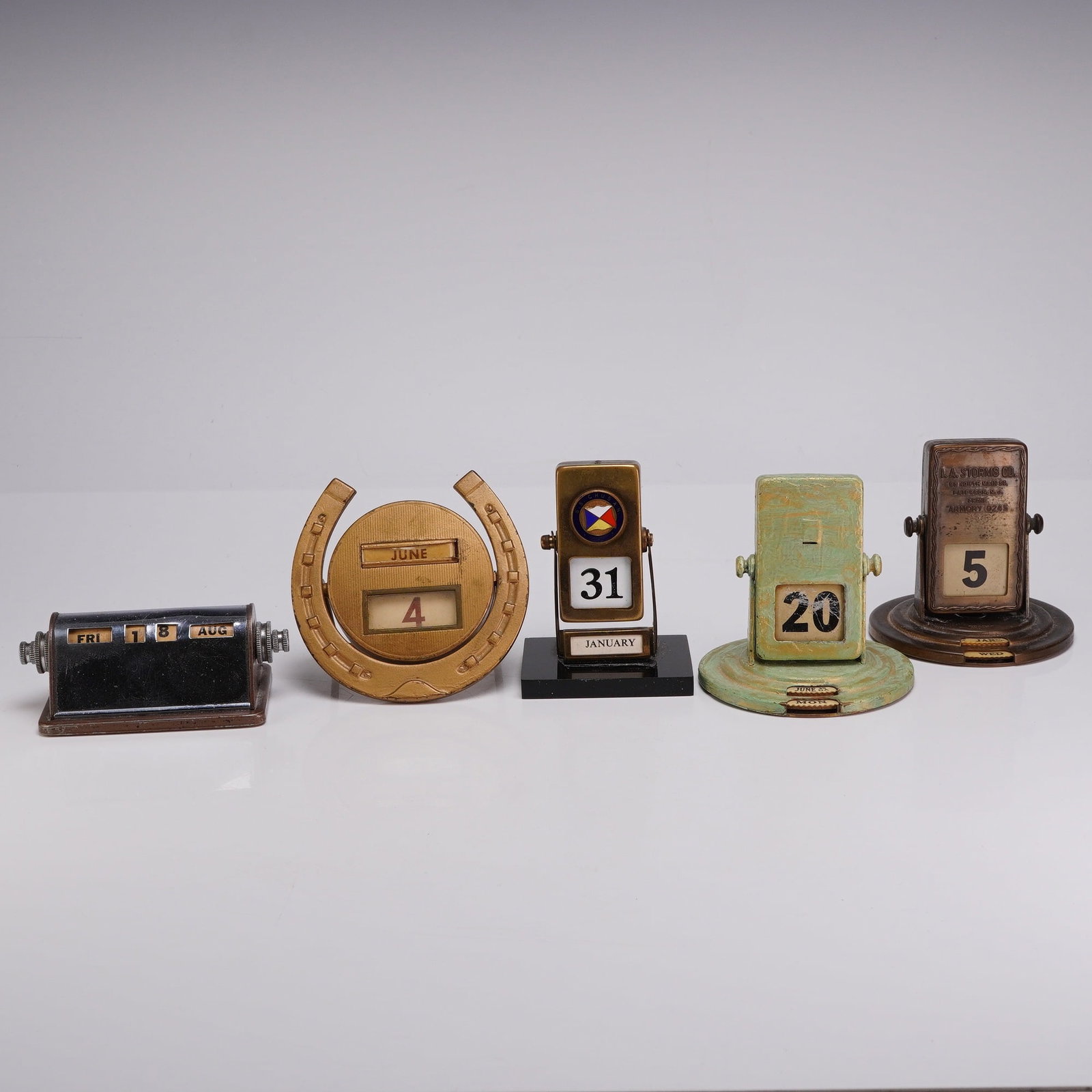 Group of Five Vintage Metal Perpetual Roll Top and Flip Desk Calendars: This collection of five vintage perpetual desk calendars includes various mechanical designs such as the 5 roll top calendar style and several flip-action models, including types attributed to makers 