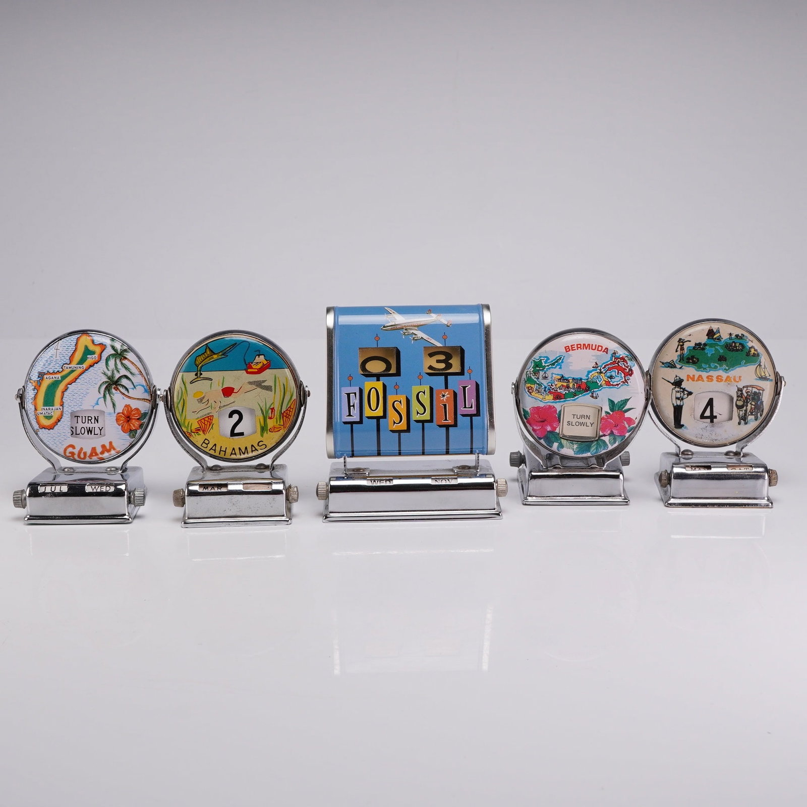 Group of Five Vintage Style Chrome Perpetual Roll Top Flip Desk Calendars: This collection consists of five mechanical perpetual roll top and flip-style desktop calendars featuring chrome-plated metal housings and printed plastic and paper components. The group includes one 