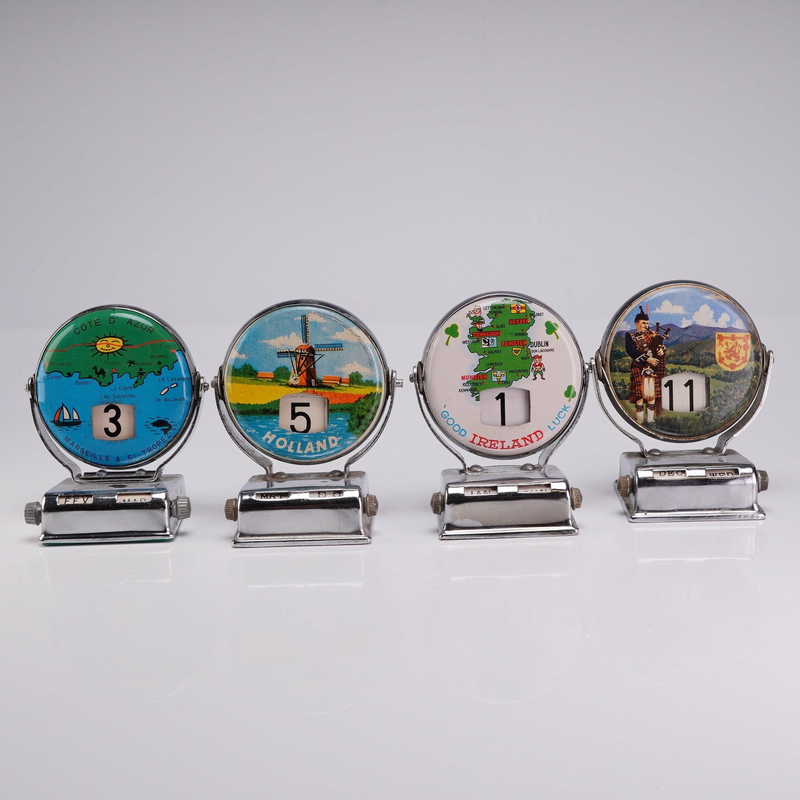 Set of 4 Vintage Metal Perpetual Flip Roll Top Desk Calendars: These mid-century souvenirs representing various European regions are constructed with a chrome-plated metal housing and a central circular body mounted on a swivel frame. The date advances by flippin