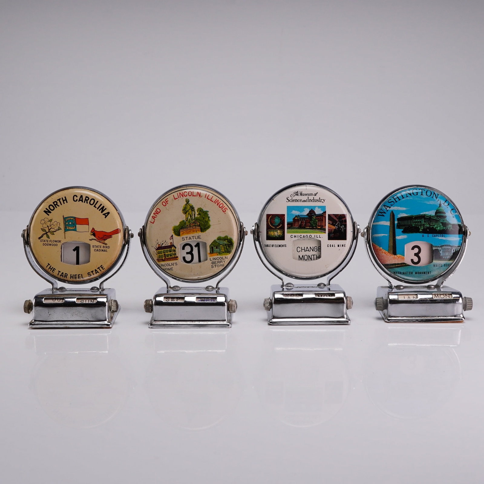 4pc Chrome Perpetual Roll Top Flip Desk Calendars: This lot consists of 4 roll top calendar units featuring a mechanical perpetual flip design. Each unit is constructed with a chrome-plated metal base and a circular rotating frame. The mechanism utili