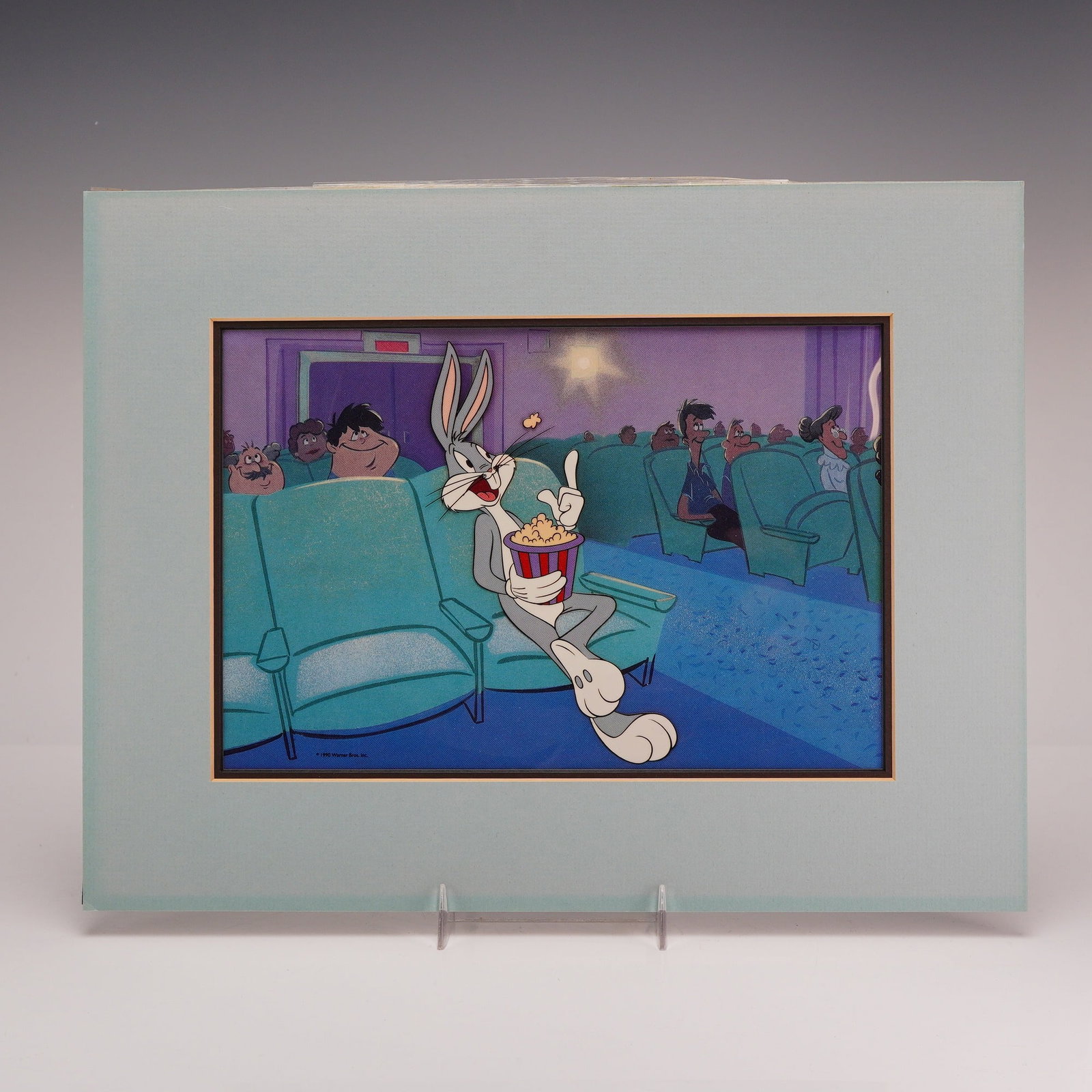 Warner Bros. Bugs Bunny At the Movies 50th Anniversary Animation Serigraph: This 1990 Warner Bros. Inc. animation serigraph, titled At the Movies, depicts the Looney Tunes character Bugs Bunny seated in a movie theater eating popcorn. The character is shown holding a red and 