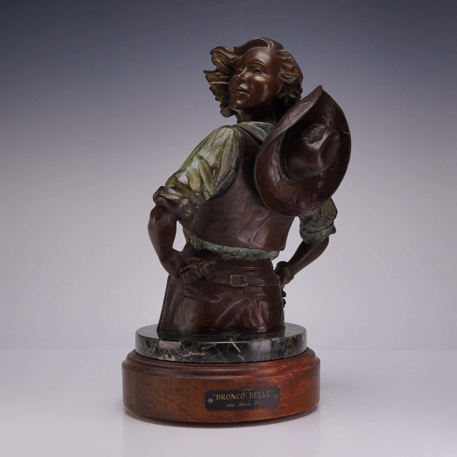 Star Liana York (American, b.1952), Bronze Bust, Bronco Belle: This contemporary polychrome bronze bust, titled Bronco Belle, is the work of artist Star Liana York. The sculpture depicts a cowgirl in a mid-turn pose, looking back over her shoulder with a wide-bri