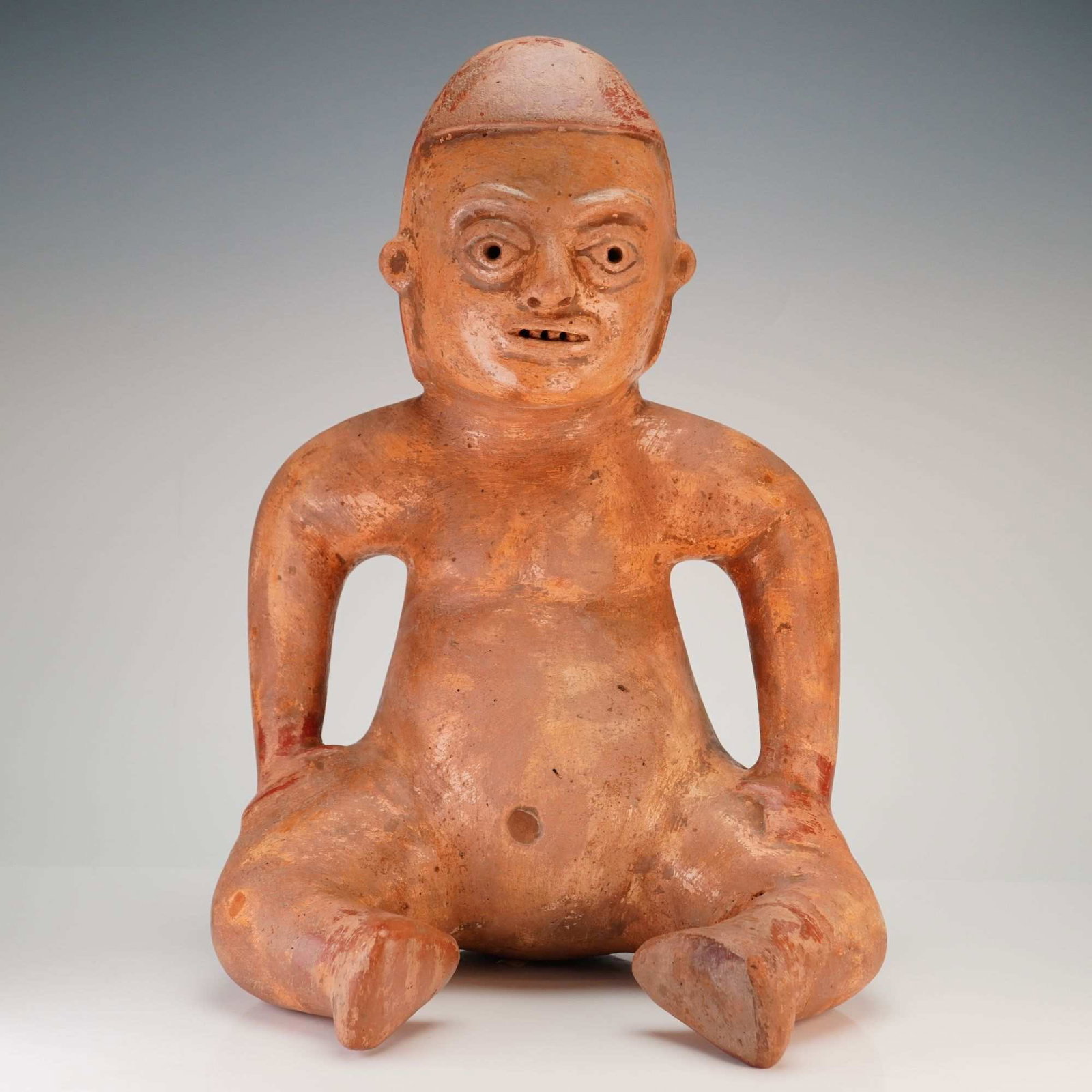 Seated Colima-Style Terracotta Sculpture with Olmecoid Features: This hollow-molded terracotta sculpture in the Colima culture style, depicts a seated male figure in the classic fat man style characteristic of Pre-Columbian art from the Protoclassic period. The fig