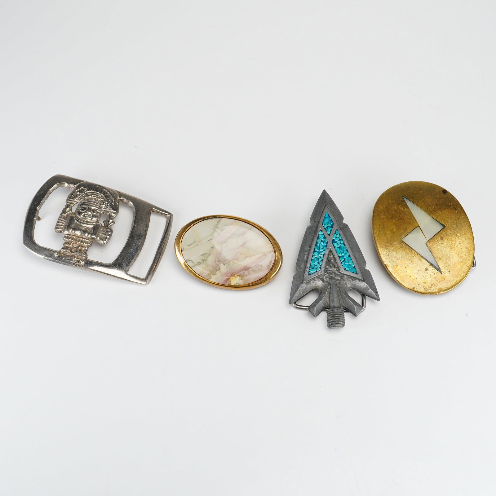 4pc Collection of Vintage Metal Belt Buckles: A collection of vintage metal belt buckles featuring varied decorative motifs and materials. The assortment includes an oval gold-tone metal buckle with a polished, multi-colored cabochon inlay, marke