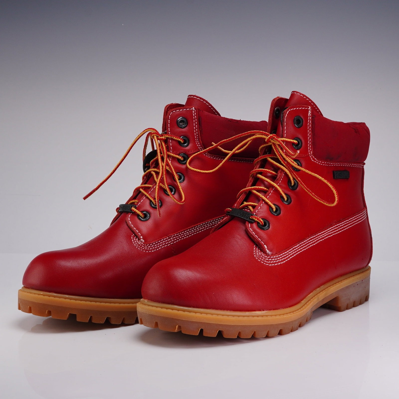 Pair of Buffalino Explorer Red Leather B-Boots: A pair of Buffalino Explorer 6-inch lace-up boots featuring bright red leather uppers with white contrast stitching. The boots are constructed with a dark red padded textile collar, seven metal eyelet