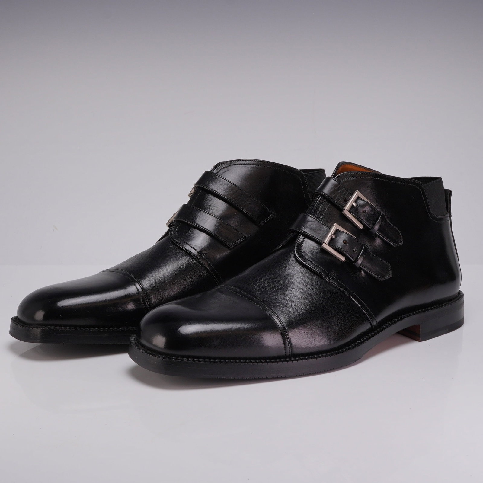 Pair of Mezlan Ferrara Black Leather Double Monk Strap Boots: This pair of Mezlan Ferrara ankle boots features a hybrid chukka-style silhouette with a double monk strap closure and silver-tone buckles. The uppers are crafted from smooth black leather with a cap 