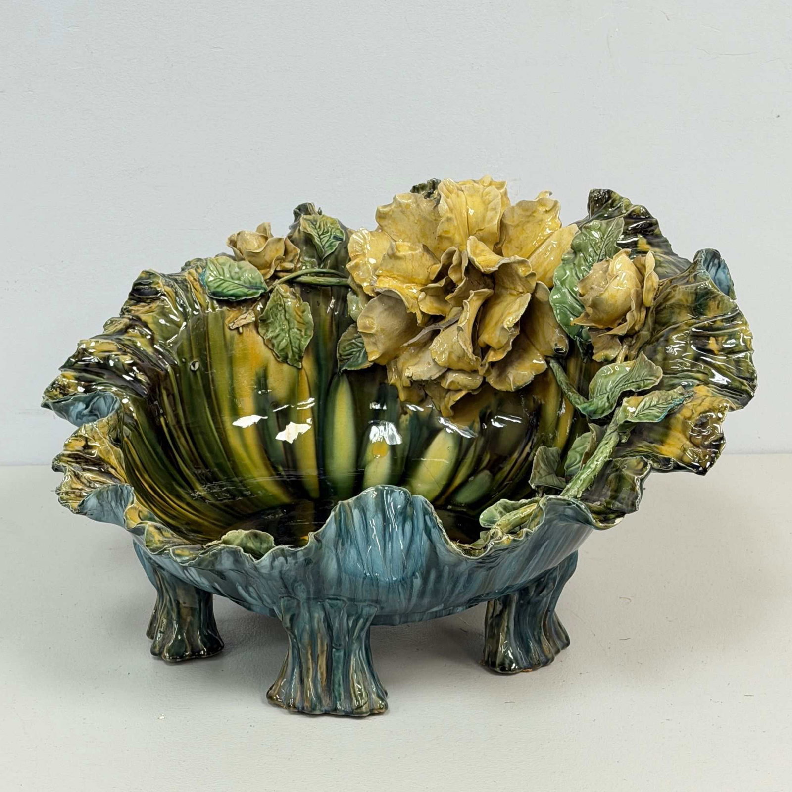 Large Majolica Barbotine Centerpiece Bowl w/ Applied Rose & Leaf Motifs: A large, footed ceramic centerpiece bowl in the barbotine majolica style. The earthenware body is naturalistically modeled as a ruffled cabbage or kale leaf, resting on four textured feet resembling t