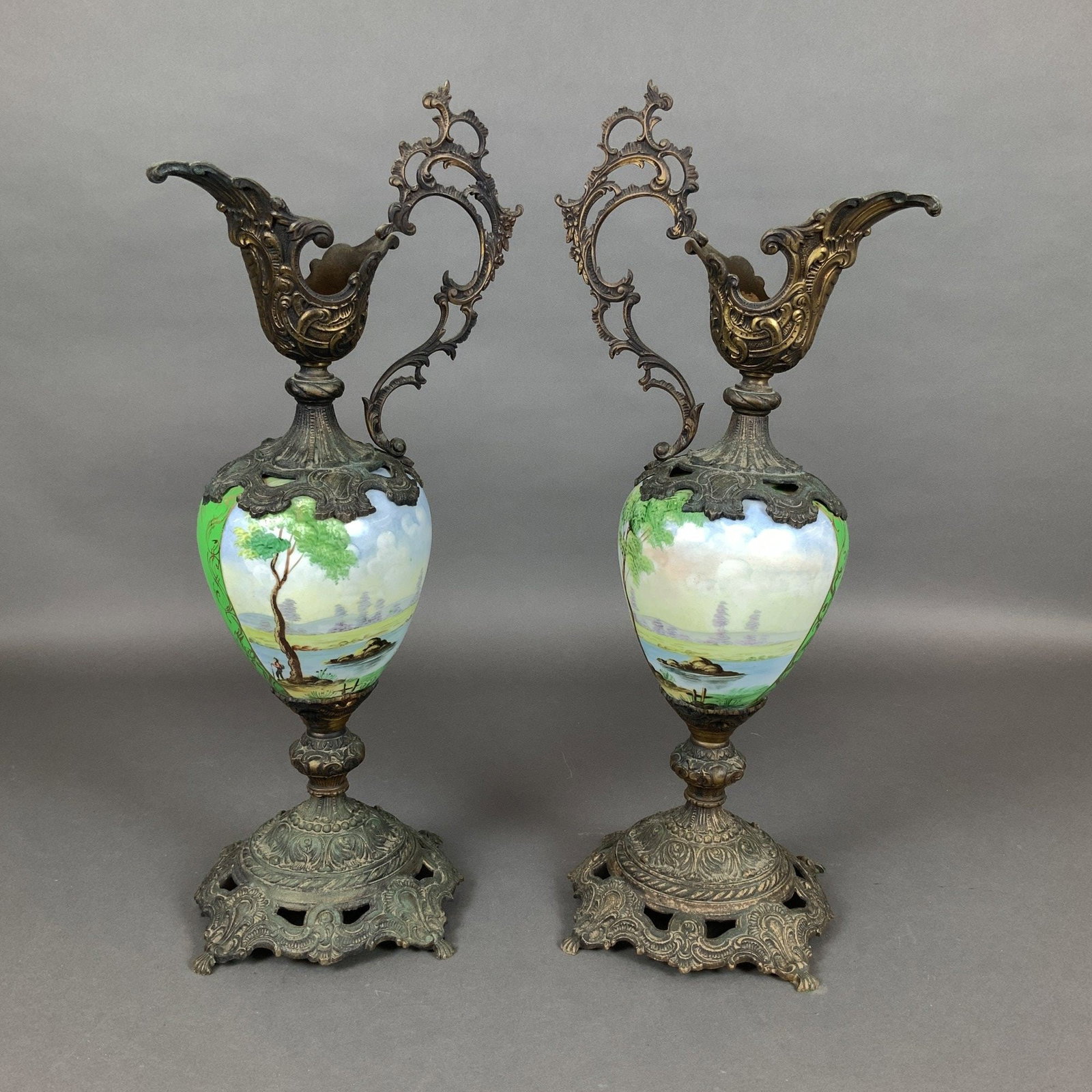 A Pair of Victorian Style Hand-Painted Ceramic and Cast Metal Mounted Ewers: This pair of metal and ceramic ewers is representative of the Rococo Revival style popular in the late 19th century. Each ewer features an ovoid ceramic body finished in a vibrant, opaque green glaze.