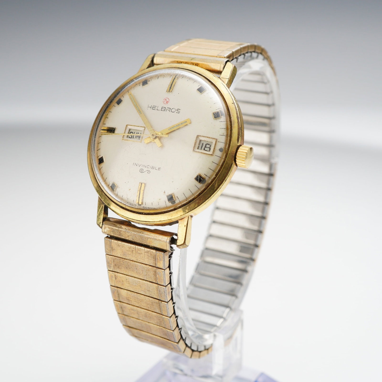 Helbros Invincible Split Window Day Date Mechanical Wristwatch: This vintage Helbros Invincible mechanical wristwatch features a distinct split window day and date complication. The watch is constructed with a 10 karat rolled gold plate bezel and a stainless steel