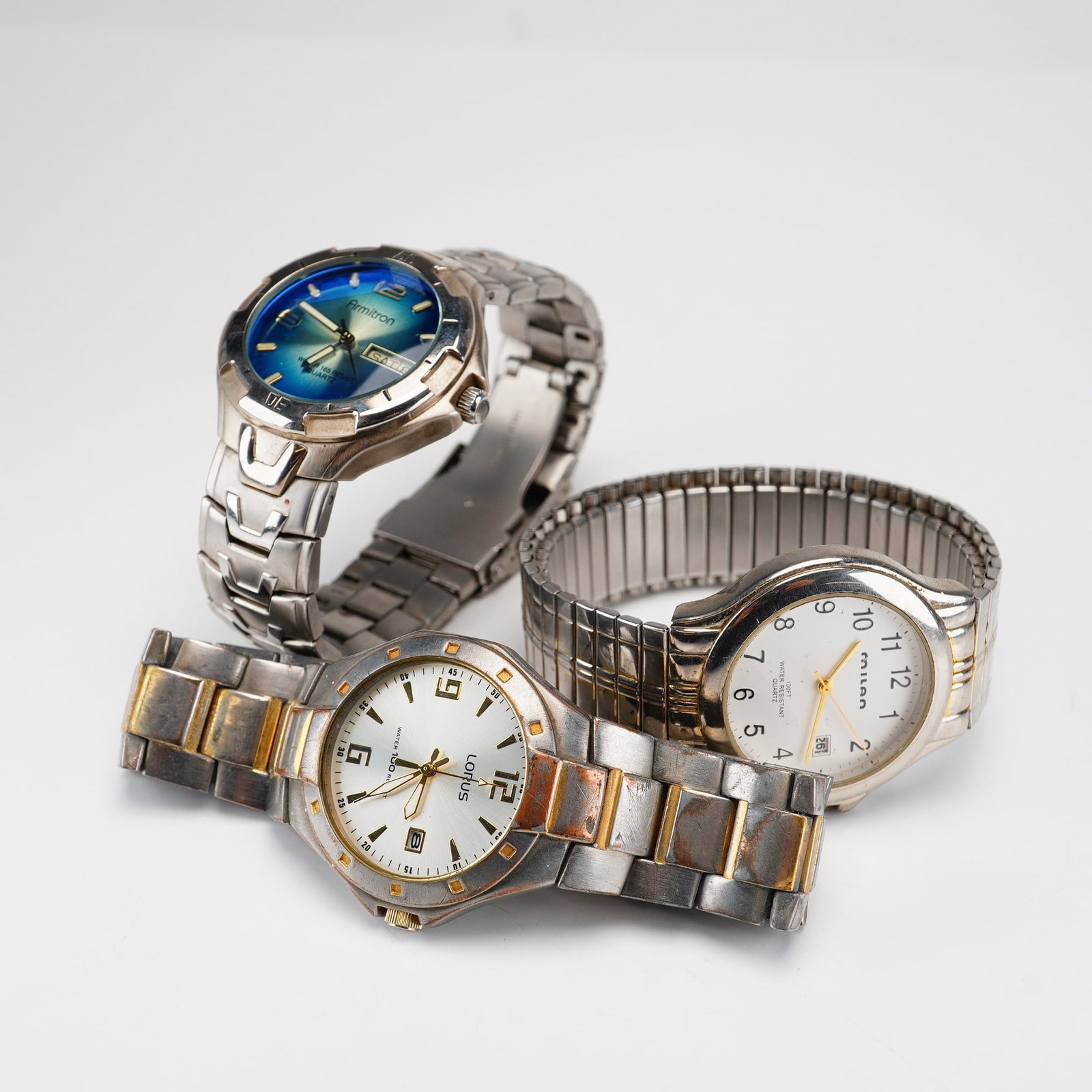 Three Quartz Wristwatches by Armitron Lorus and Milan: This lot consists of three silver and gold toned band watches in various styles. The first is an Armitron quartz wristwatch, model 20/1823, featuring a blue-to-green sunburst gradient dial with a day 