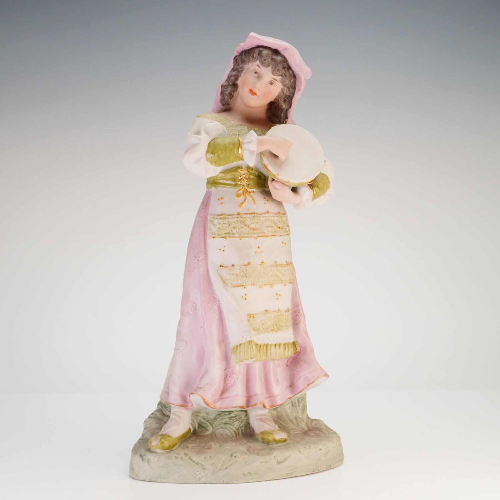 Gebruder Heubach German Bisque Figurine, Woman with Tambourine: A hand-painted bisque porcelain figurine of a young woman in traditional European folk attire by Gebruder Heubach. The figure is depicted standing on a naturalistic base with a mossy texture. She wear