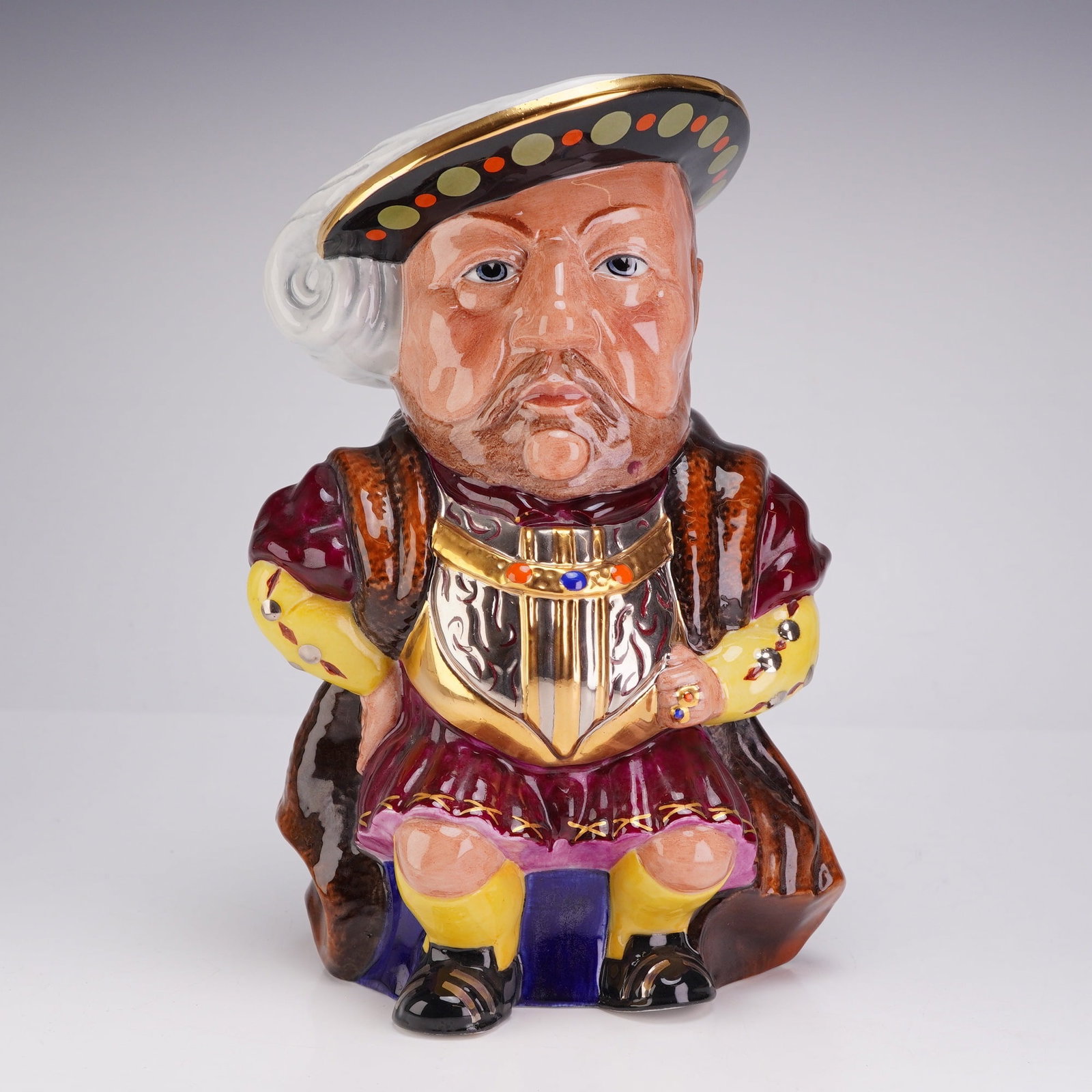 Staffordshire Fine Ceramics King Henry VIII Limited Edition Toby Jug: A Staffordshire Fine Ceramics polychrome glazed ceramic Toby jug depicting King Henry VIII. The seated figure is portrayed in Tudor attire, featuring a wide-shouldered, brown fur-trimmed cloak over a 
