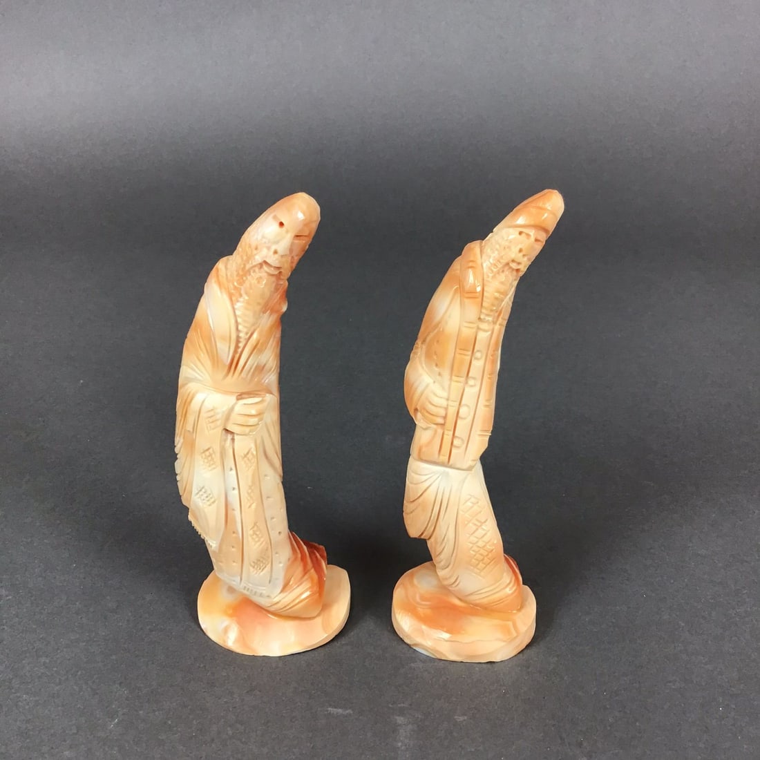 Pair of Chinese Carved Coral Figurines: A pair of Chinese carved coral figurines depicting elderly men or sages in traditional East Asian attire. Each figure is hand-carved in a leaning or bowing posture that follows the natural curvature o