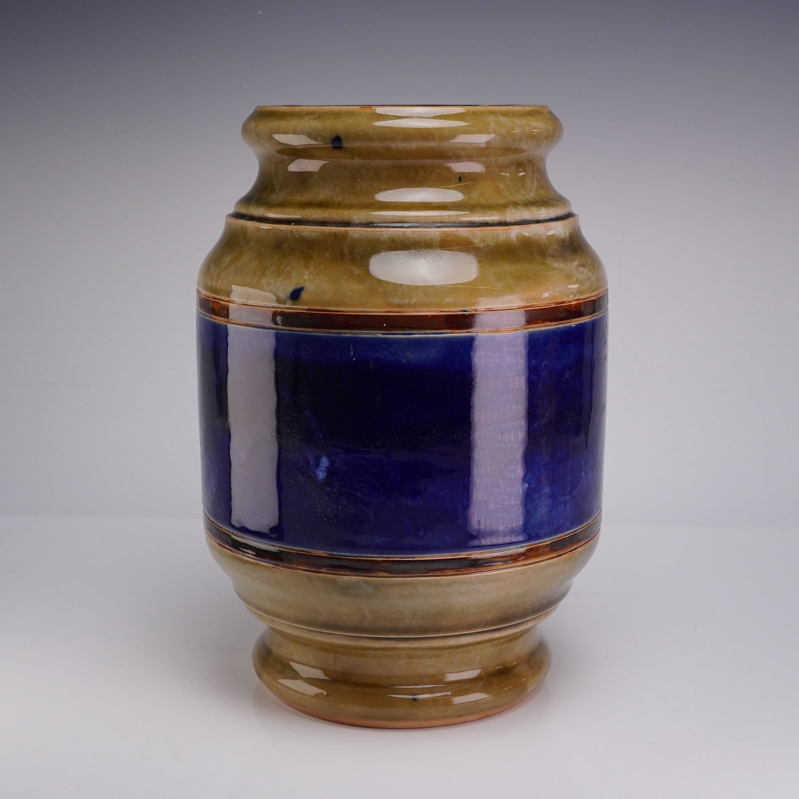 Royal Doulton Stoneware Tobacco Humidor with Cobalt Blue Band: This is a cylindrical tobacco humidor produced by Royal Doulton. The piece is constructed from high-fired stoneware, characteristic of the Doulton Lambeth studio. It features a wide, slightly recessed