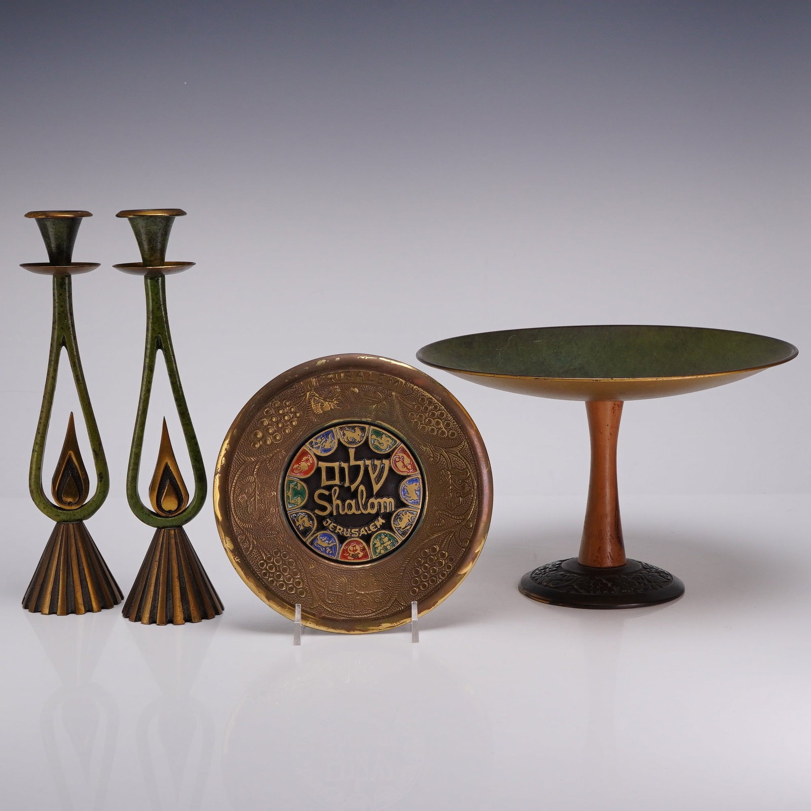 Collection of Four Mid-Century Modern Israeli Brass and Enamel Judaica Items: A collection of four mid-century modern Israeli brass and enamel Judaica items. The lot includes a pair of modernist Shabbat candlesticks featuring teardrop-shaped open frames on fluted, conical bases