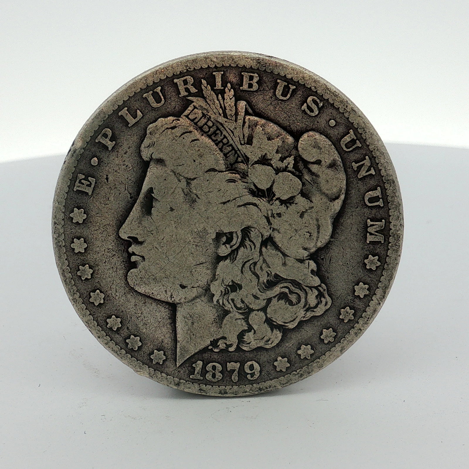 1879 US One Dollar Morgan Silver Dollar, Circulated: This US Morgan silver dollar was struck at the Philadelphia Mint in 1879. The coin is composed of 90 percent silver and 10 percent copper. The obverse features the Liberty head design, and the reverse