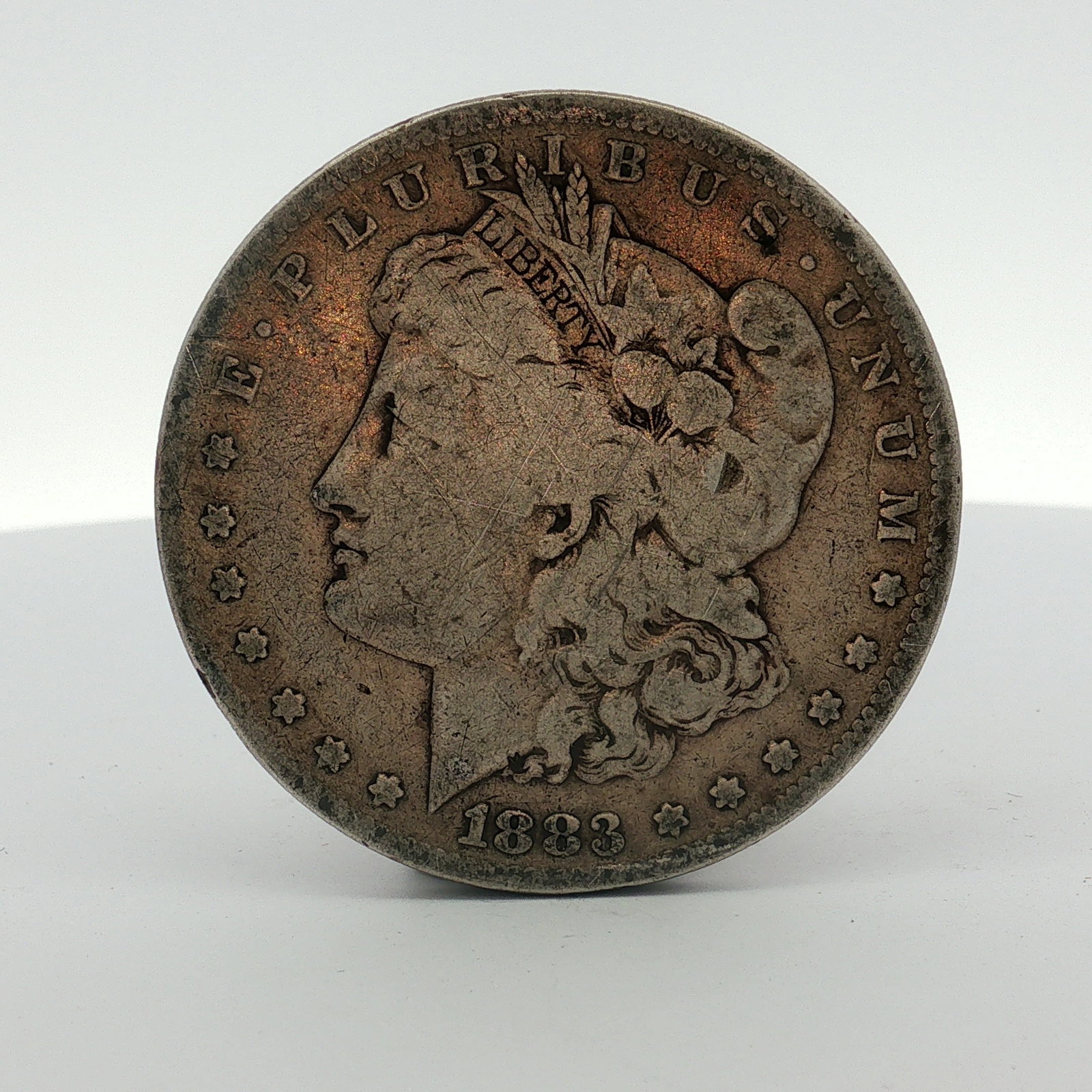 1883-S US One Dollar Morgan Silver Dollar, Circulated: This coin was struck at the San Francisco Mint and features a reeded edge. The obverse includes the date 1883 and the legend E PLURIBUS UNUM. The reverse includes the inscriptions UNITED STATES OF AME