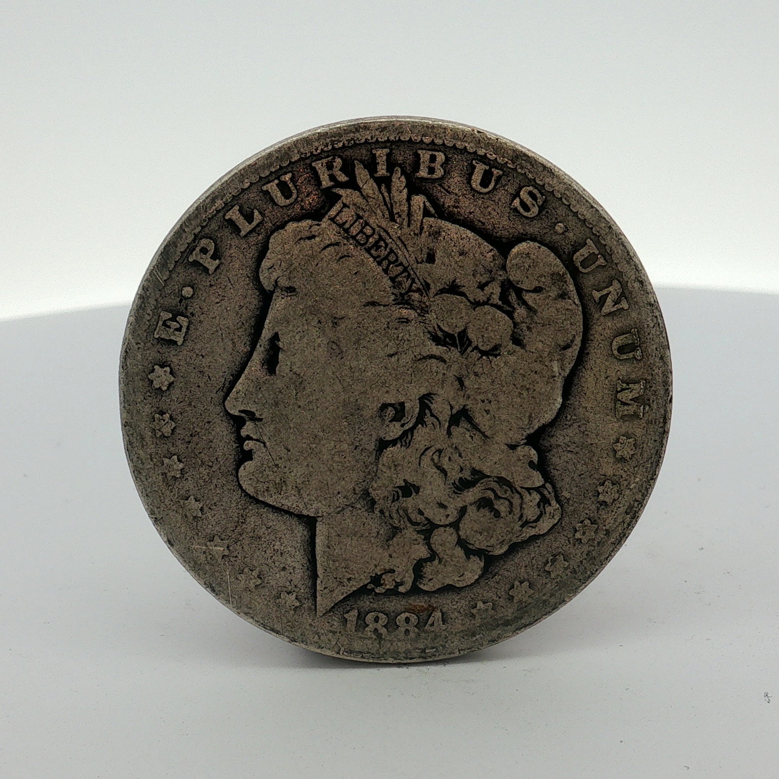 1884 US Morgan Silver Dollar Coin Circulated: This US 1884 Morgan silver dollar was struck at the Philadelphia Mint. The coin features the Morgan dollar design. The obverse includes the date 1884 and the legend E PLURIBUS UNUM. The reverse featur
