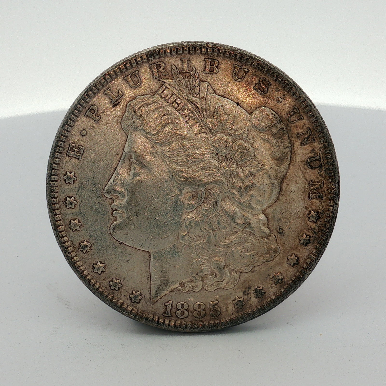 1885 US One Dollar Morgan Silver Dollar, Circulated: This US 1885 Morgan silver dollar was produced at the Philadelphia Mint. The specimen is struck in .900 fine silver. The coin features a reeded edge and bears the inscriptions E PLURIBUS UNUM, 1885, U
