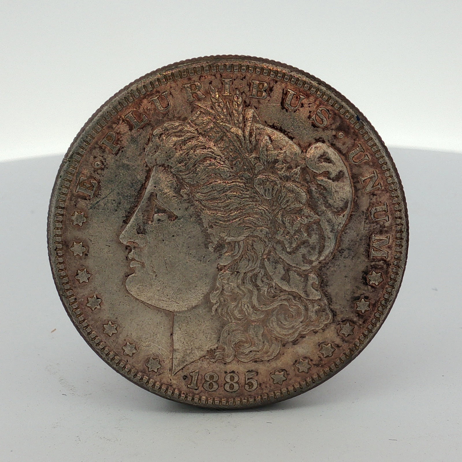 1885 US One Dollar Morgan Silver Dollar, Circulated: This 1885 US Morgan silver dollar was struck at the Philadelphia Mint. The coin is composed of 90% silver and 10% copper. It features the Morgan dollar obverse and reverse design types with a reeded e