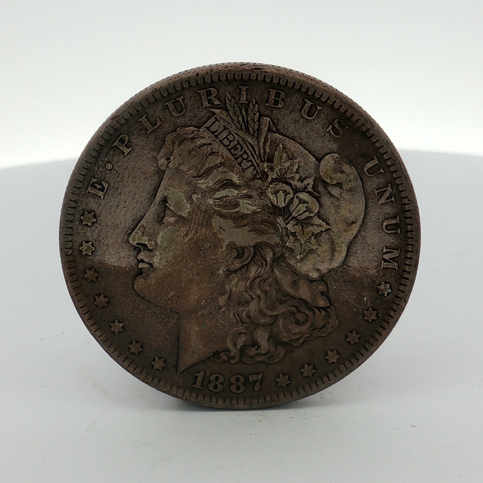 1887 US Morgan Silver Dollar Coin Circulated: This 1887 US Morgan silver dollar was struck at the Philadelphia Mint. The coin is composed of 90 percent silver and 10 percent copper. The obverse features the Morgan Liberty head design with the leg