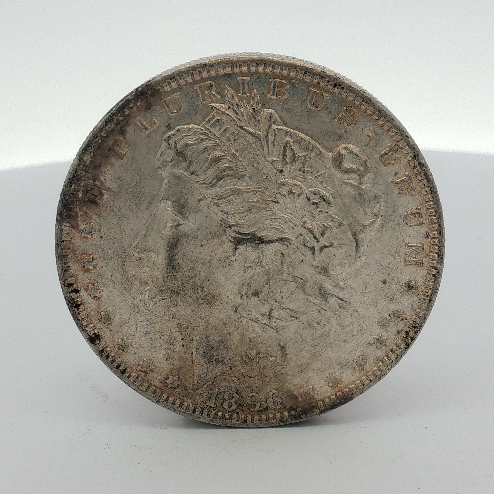 1896 US One Dollar Morgan Silver Dollar, Circulated: This US Morgan dollar was struck at the Philadelphia mint in 1896. The coin is composed of 90 percent silver and 10 percent copper. The obverse features the Liberty head design with the headband inscr