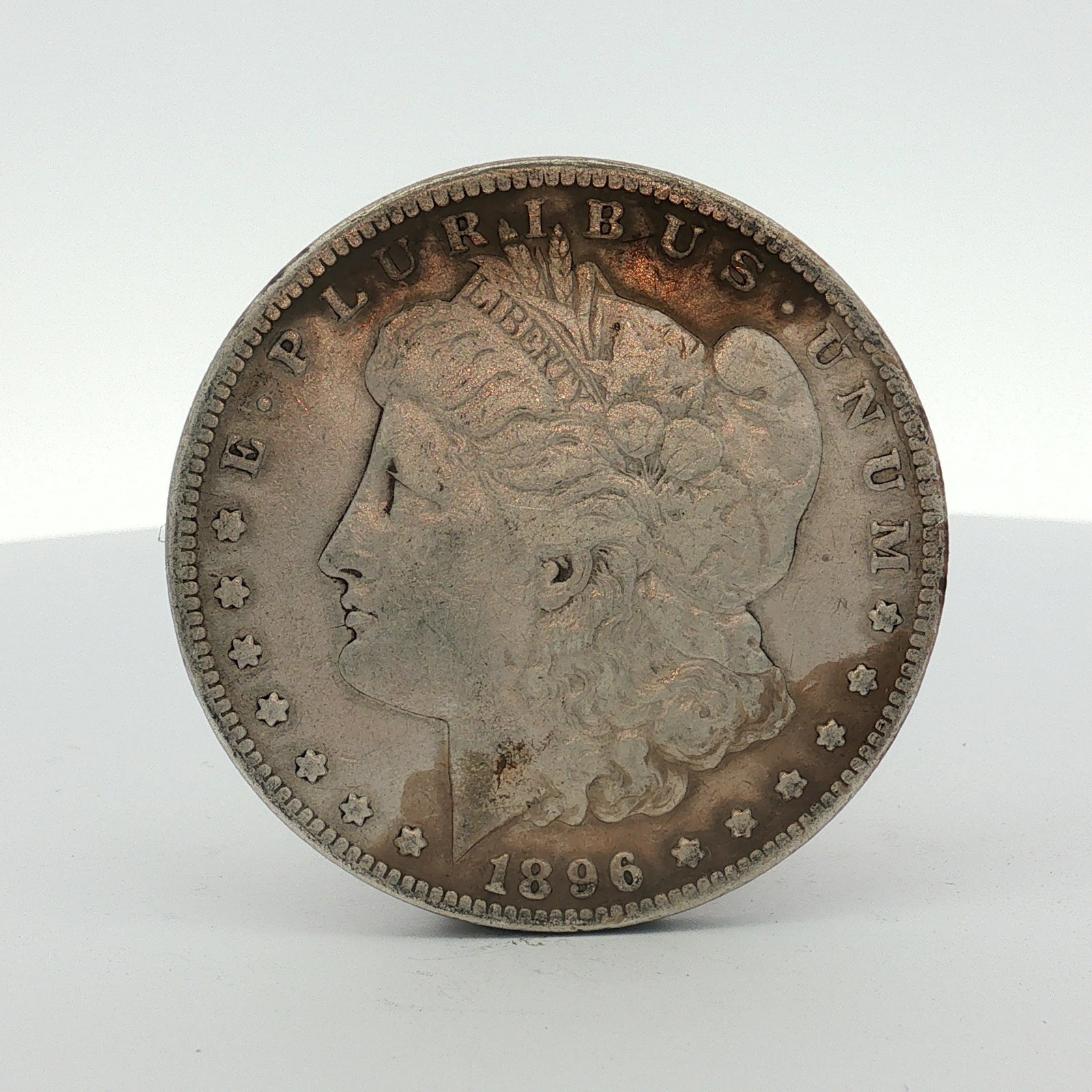 1896-S US One Dollar Morgan Silver Dollar, Circulated: This US silver coin is a Morgan dollar struck at the San Francisco Mint in 1896. The piece is composed of 90% silver and 10% copper. It features the Liberty Head obverse and the Eagle with Wreath reve