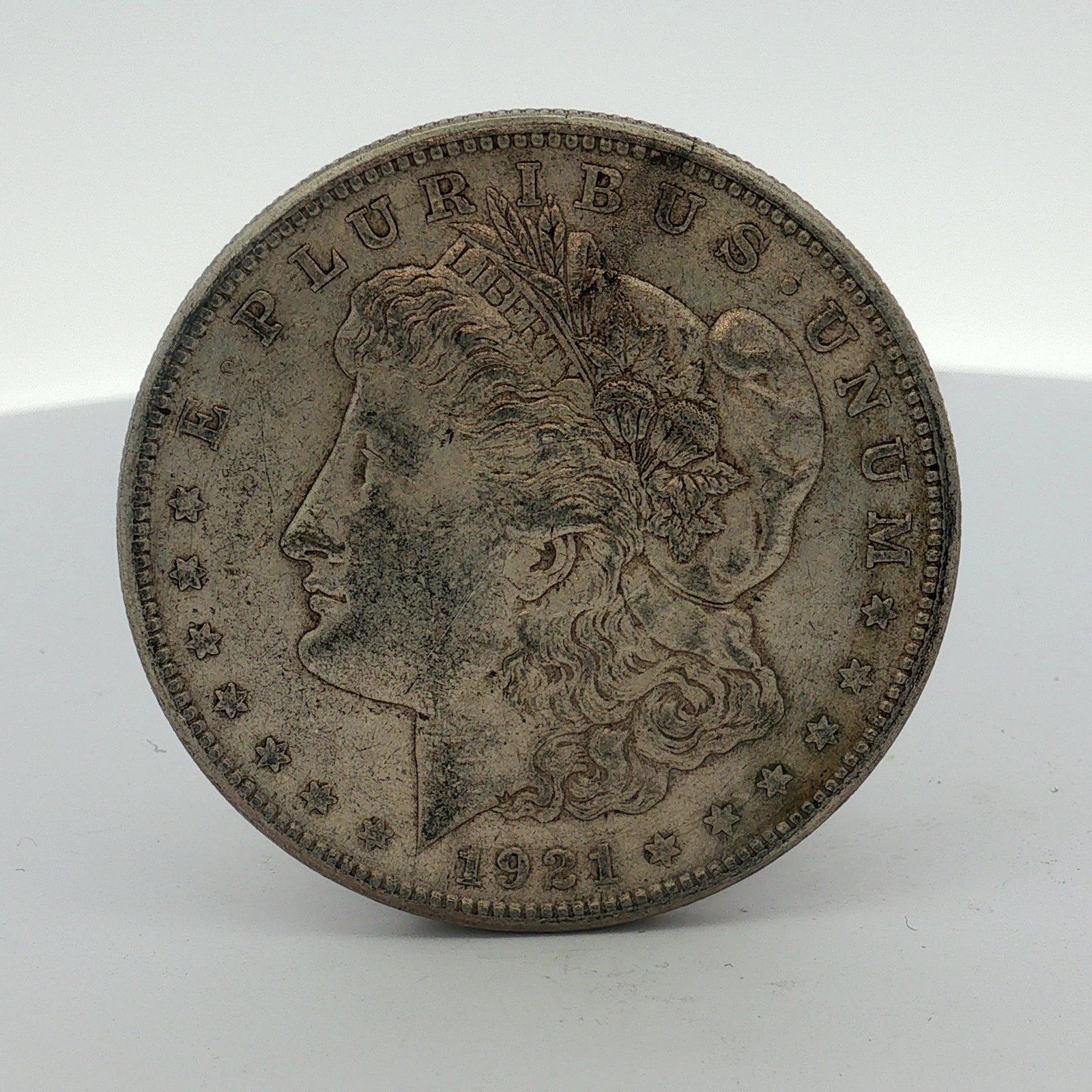 1921 US Morgan Silver Dollar Coin Circulated: This 1921 US Morgan Silver Dollar was struck at the Philadelphia Mint. The coin is composed of .900 fine silver. The obverse features the Liberty head design with the motto E PLURIBUS UNUM and the dat