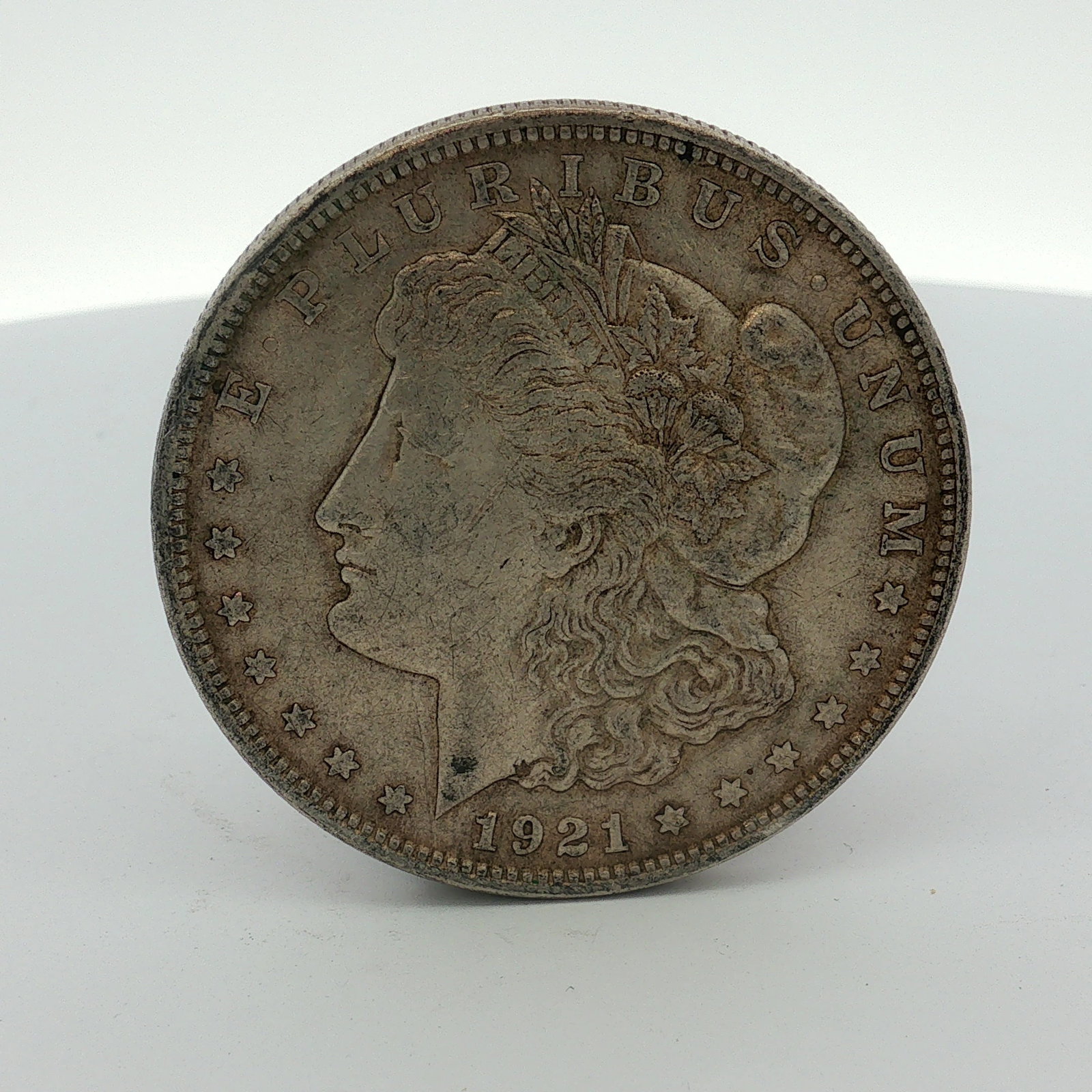 1921 US One Dollar Morgan Silver Dollar, Circulated: This US Morgan silver dollar was struck at the Philadelphia Mint in 1921. The coin is composed of 90 percent silver and 10 percent copper. The obverse features the Morgan dollar Liberty head design wi