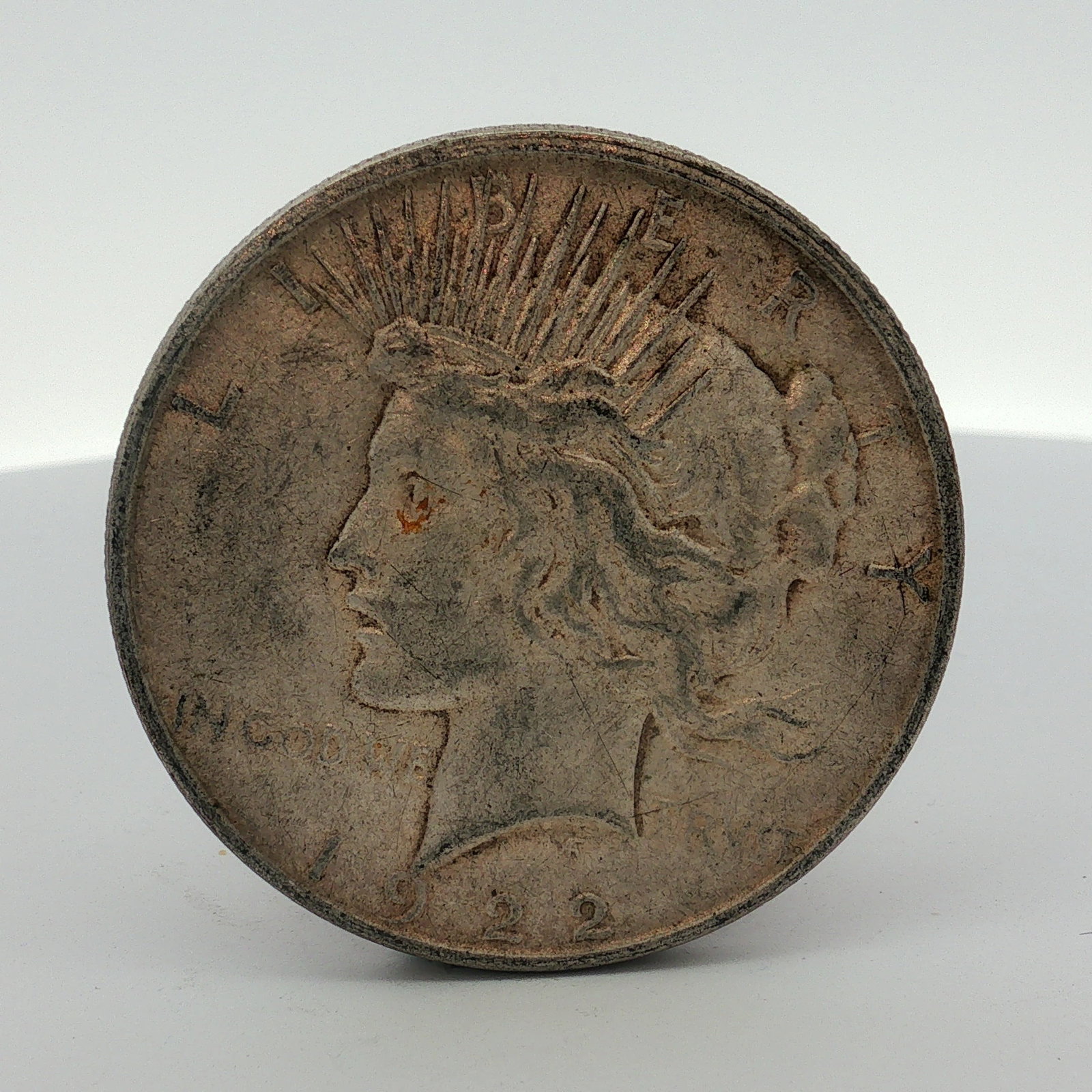 1922-D US One Dollar Peace Silver Dollar, Circulated: This Peace dollar is a US silver coin struck at the Denver Mint in 1922. The coin features a reeded edge. The obverse features the Peace dollar obverse design with the inscriptions LIBERTY, IN GOD WE 