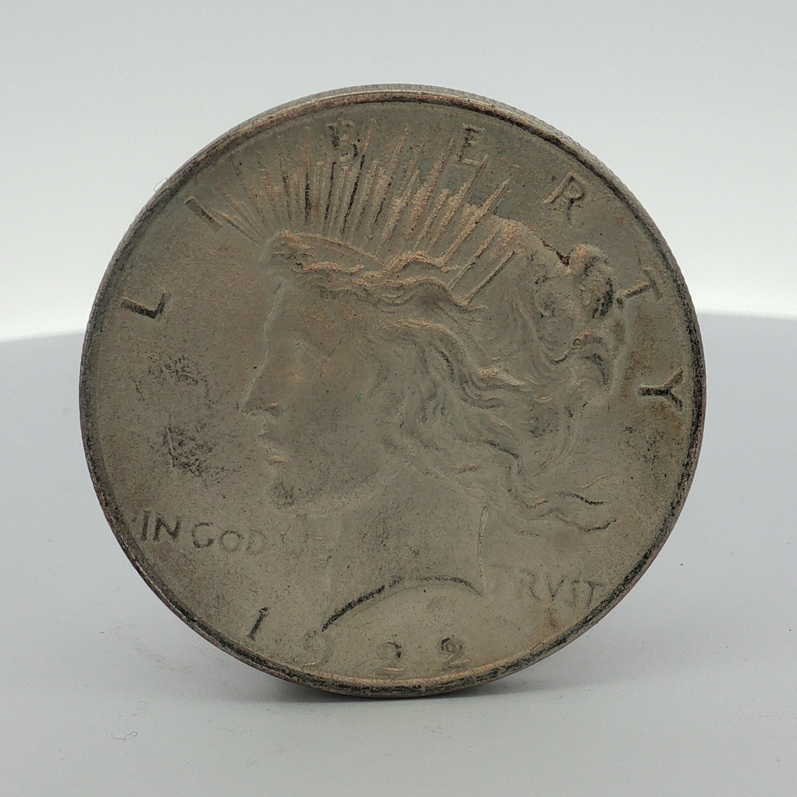 1922-D US One Dollar Peace Silver Dollar, Circulated: 1922-D US Peace silver dollar struck at the Denver Mint. This struck silver coin features the Peace dollar obverse and reverse designs. Obverse inscriptions include LIBERTY, IN GOD WE TRVST, and the d