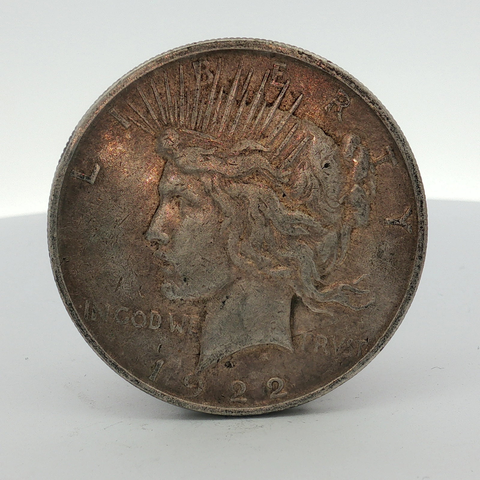 1922-D US One Dollar Peace Silver Dollar, Circulated: This US 1922-D Peace silver dollar is a Denver Mint issue. The coin features the Peace dollar obverse and reverse designs. Inscriptions include LIBERTY, IN GOD WE TRVST, and the date 1922 on the obver