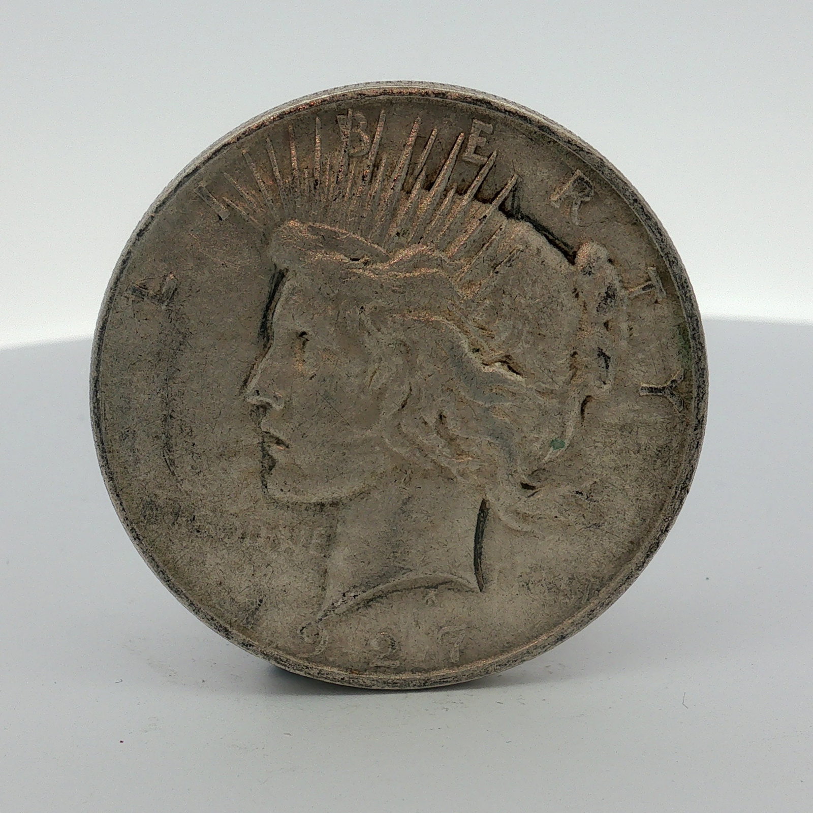 1927-D US One Dollar Peace Silver Dollar, Circulated: US 1927-D Peace silver dollar struck at the Denver mint. This currency issue coin is composed of 0.900 fine silver and 0.100 copper. The obverse features the Peace dollar design with the inscriptions 