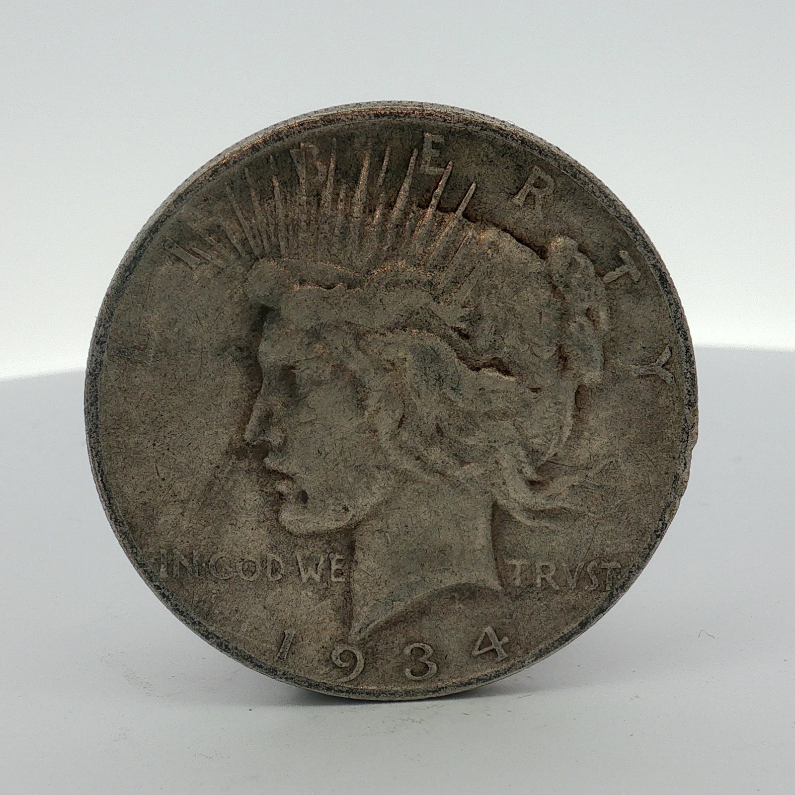 1934-D US One Dollar Peace Silver Dollar, Circulated: This 1934 US Peace silver dollar was struck at the Denver Mint. The coin features the Peace dollar obverse and reverse designs. The D mint mark is visible on the reverse to the left of the eagle's tai