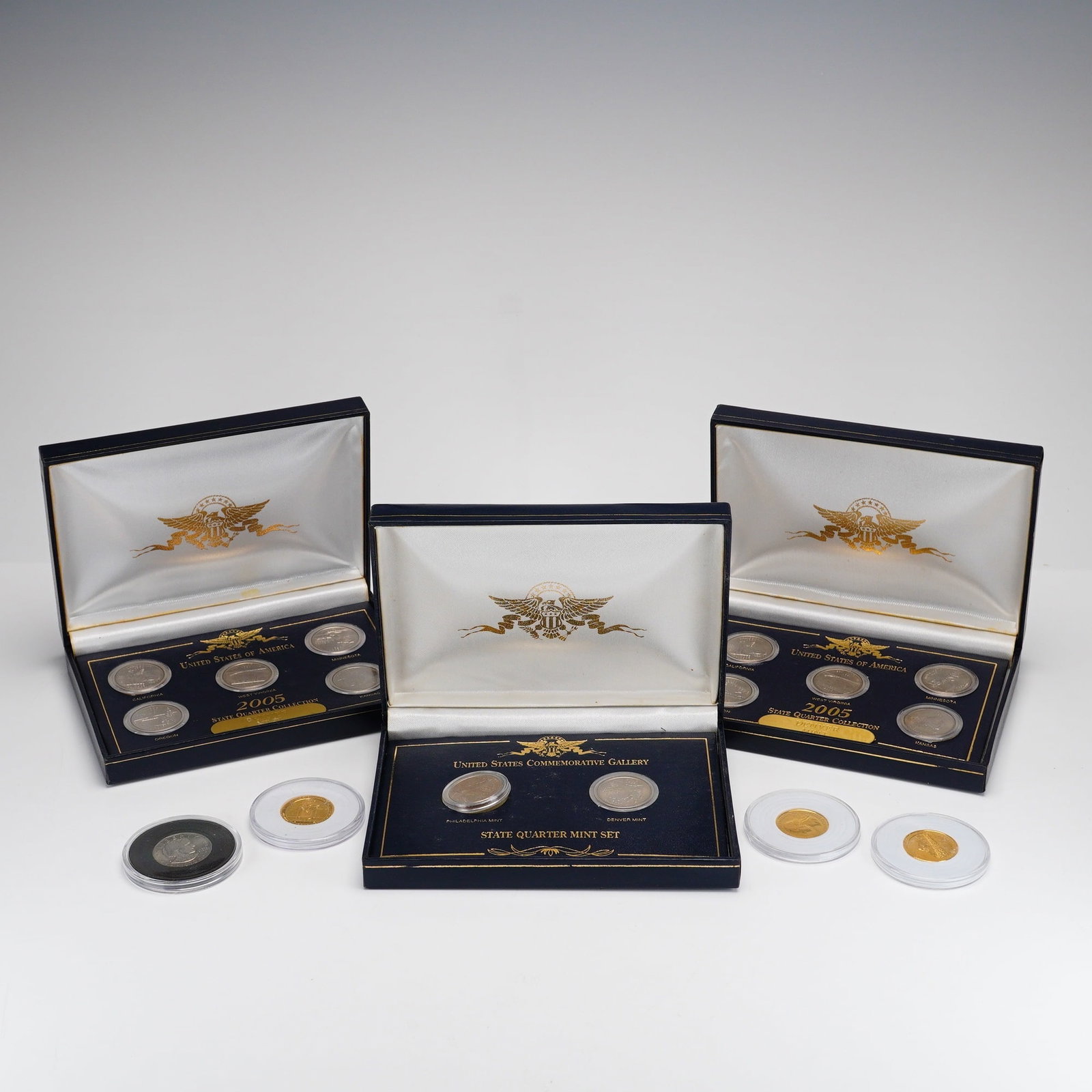 Lot of 7 2005 US State Quarter Collection, 2002 State Quarter Mint Set and 4 Coins in Sleeves: A collection of US numismatic items comprising 3 US State Quarter collection sets and 4 individual quarters and dollar coins. The group includes TWO 2005 State Quarter Collection sets from the Denver 