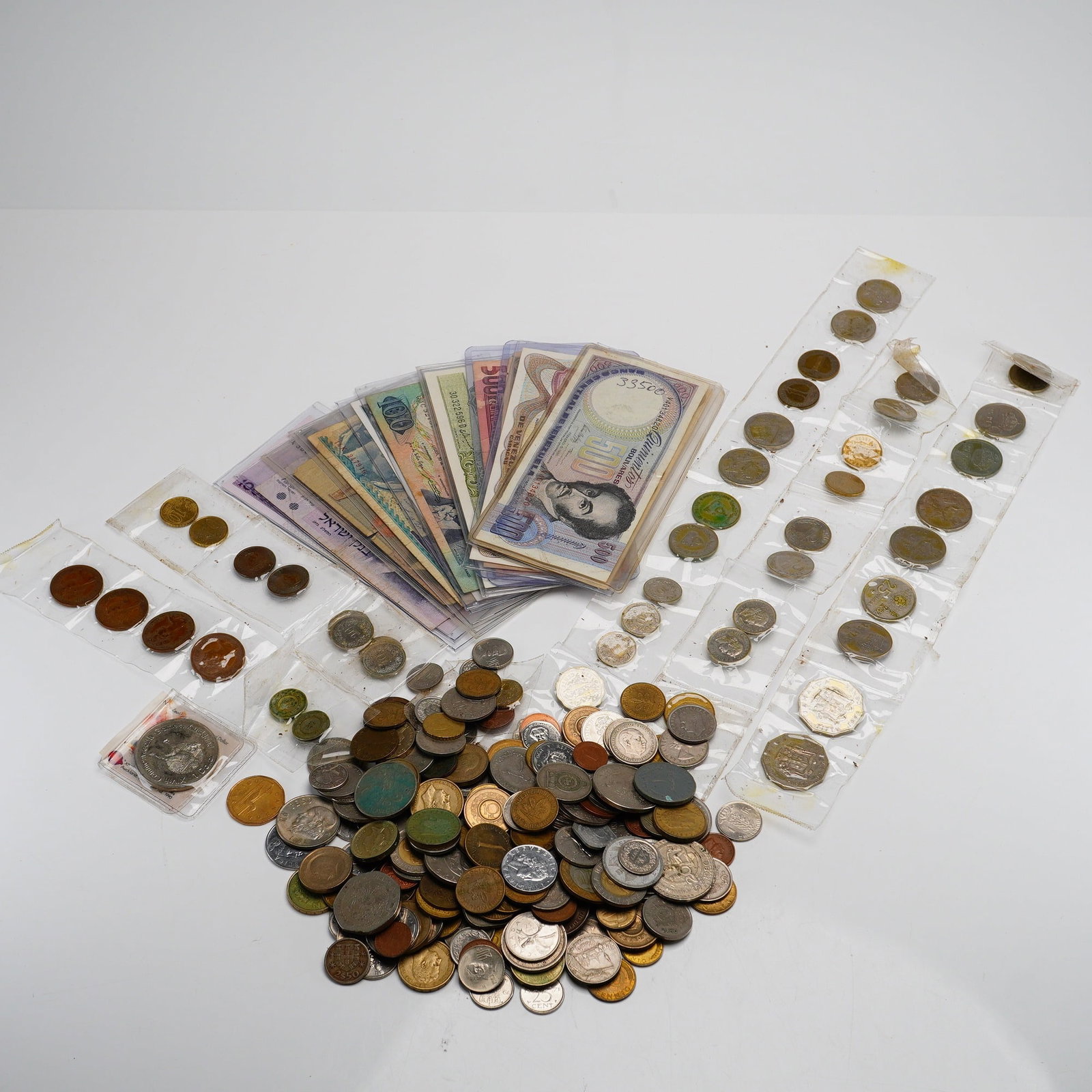 Collection of World Banknotes and a Bag of Mixed Date Foreign Currency and Coins: This lot consists of an international currency collection featuring multiple world banknotes and a large assortment of world coins. The paper currency is fanned in protective plastic sleeves and inclu