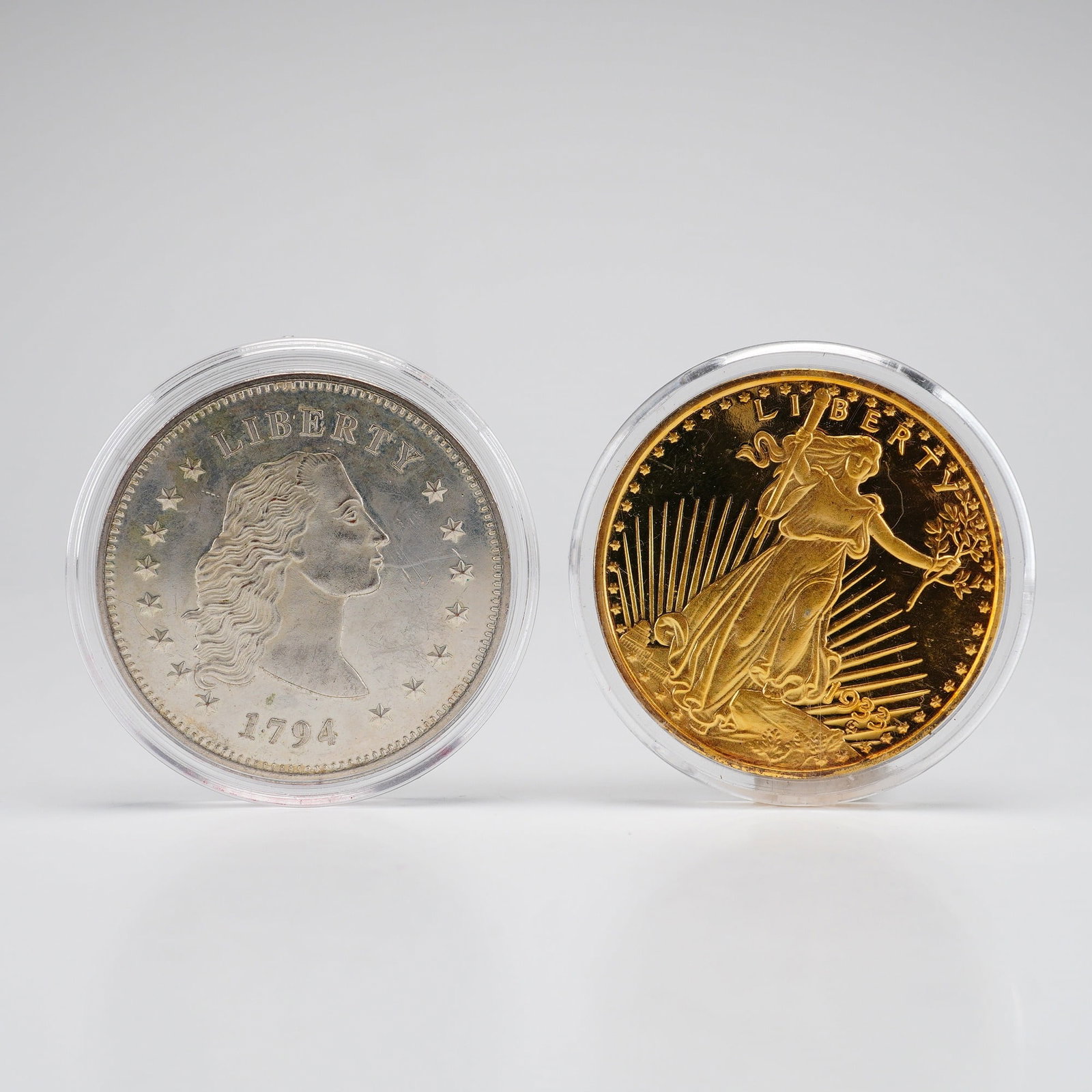 Two US American Reproductions Mint Gold Dream Collection Commemorative Coins: This lot features two numismatic reproductions from the American Mint Gold Dream collection, both presented in individual clear plastic capsules. The first item is a silver-toned replica of a 1794 US 