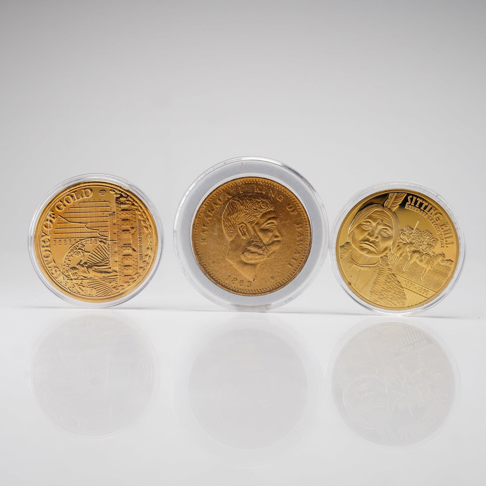 Three American Mint Commemorative Gold-Finished Rounds: This collection consists of three gold-finished commemorative rounds produced by the American Mint, each housed in a protective plastic capsule. The first round is from the Native American Chiefs seri