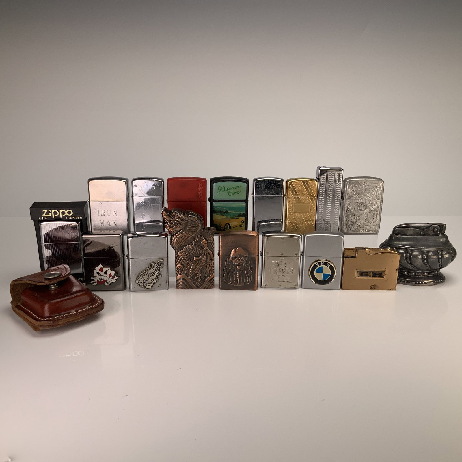 18pc Zippo and Ronson Lighters and Leather Zippo Case: An 18pc collection of pocket lighters and one table lighter, featuring Zippo and Ronson brand names. The Zippo windproof lighters, manufactured in Bradford, Pennsylvania, are presented in various fini