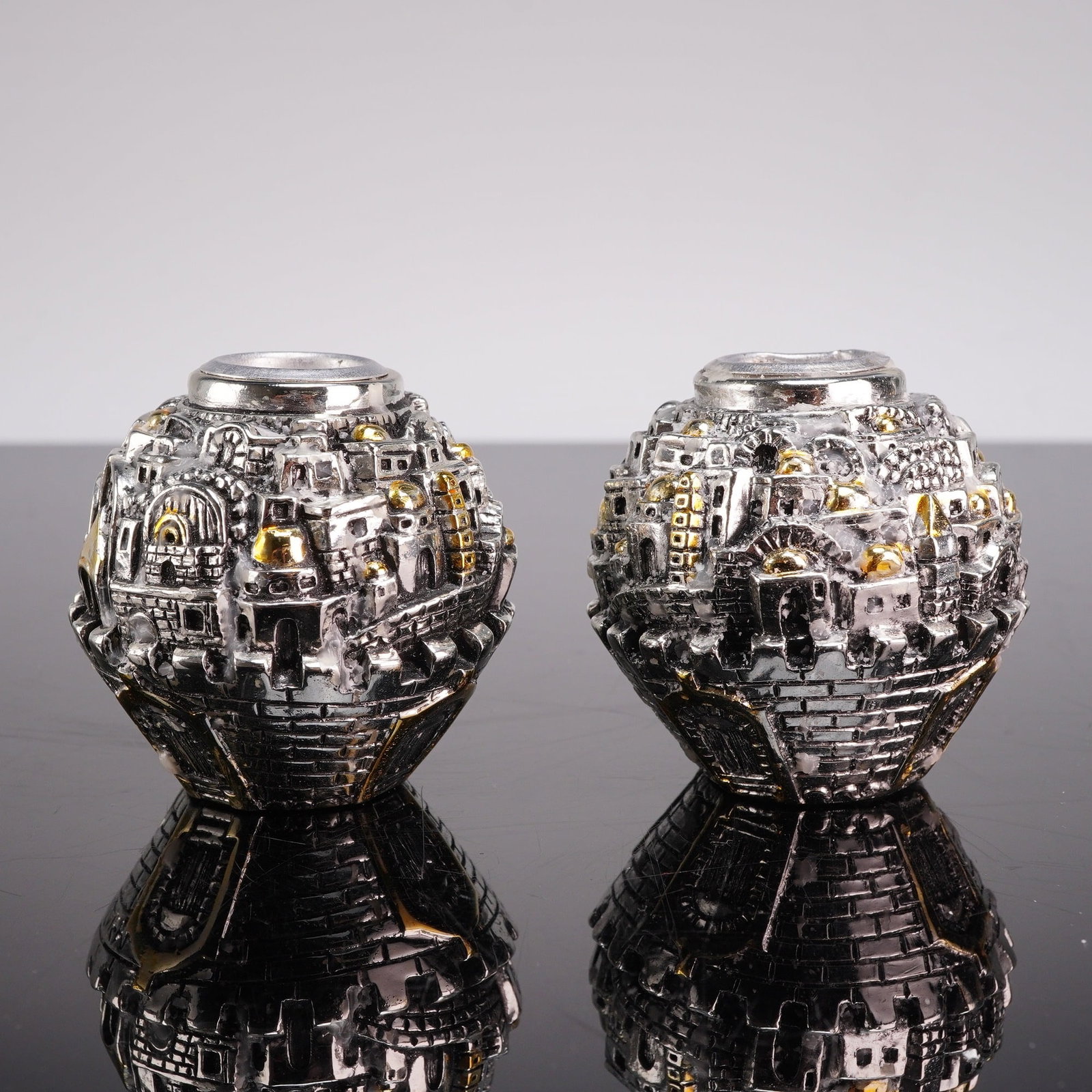 Pair of Amy Judaica Sterling Silver Jerusalem Cityscape Candle Holders: A pair of electroformed sterling silver candle holders by Amy, featuring a spherical form decorated with an intricate, three-dimensional relief of the Jerusalem cityscape. The architectural detail inc