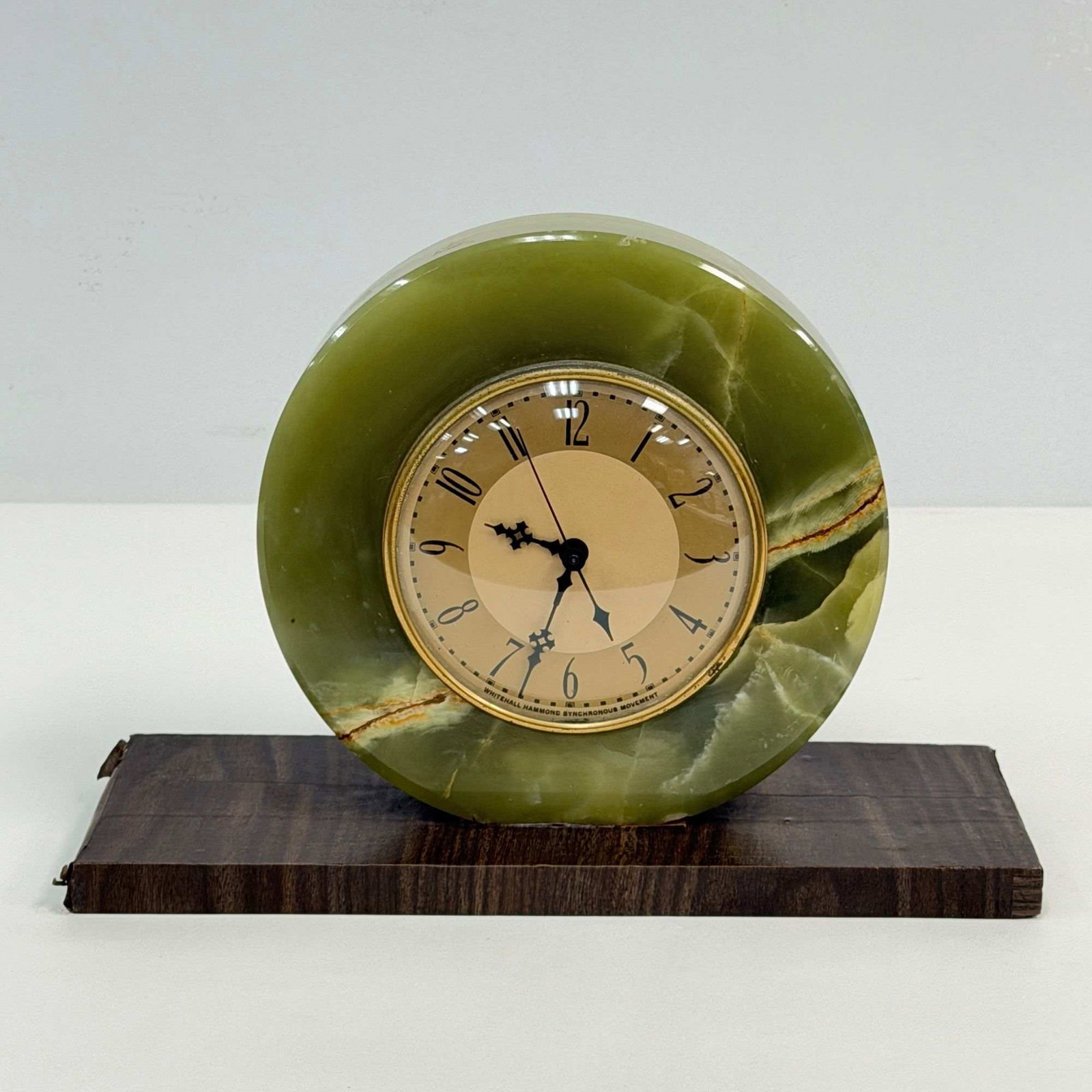 Whitehall Hammond Art Deco Green Onyx Electric Mantel Clock: An Art Deco electric mantel clock featuring a Whitehall Hammond synchronous movement. The timepiece is constructed with a circular carved green onyx stone case and a brass bezel. It is mounted to a re