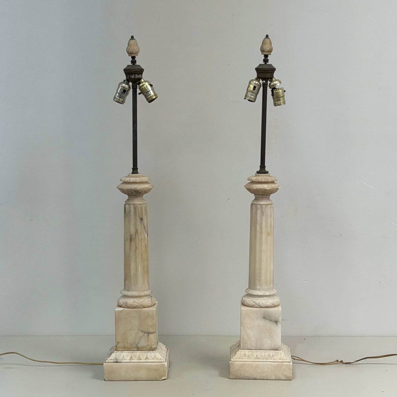 Pair of Neoclassical Carved Marble Column Table Lamps: A set of two Neoclassical-style table lamps featuring carved marble bodies in the form of fluted columns. Each lamp is set upon a square, tiered base decorated with foliate-carved borders. The lamps a