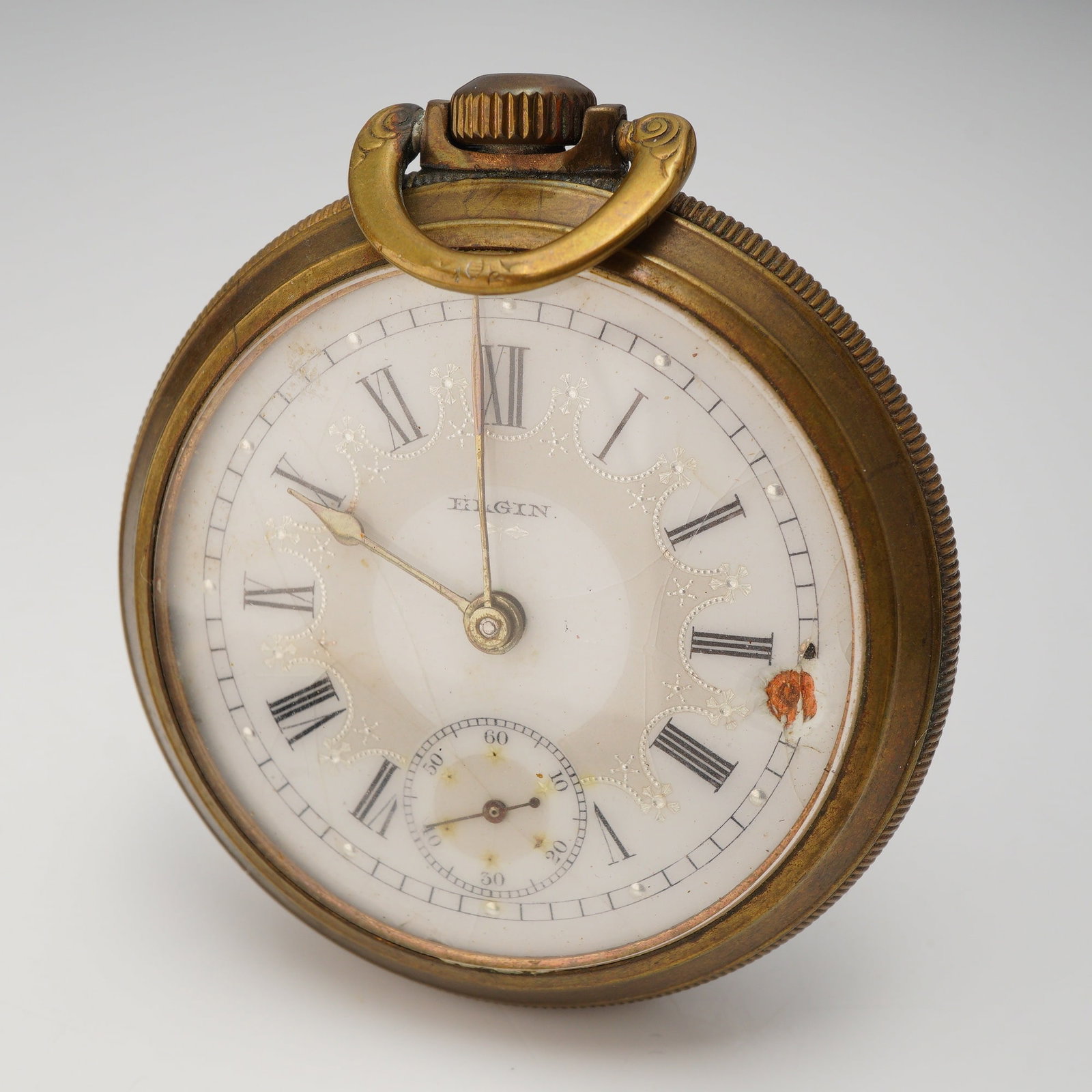 Elgin Open-Face Pocket Watch with Roman Numeral Dial: An open-face pocket watch manufactured by Elgin. The watch features a brass-toned metal case with a fluted coin-edge design on the outer band. The white dial is decorated with raised white floral and 