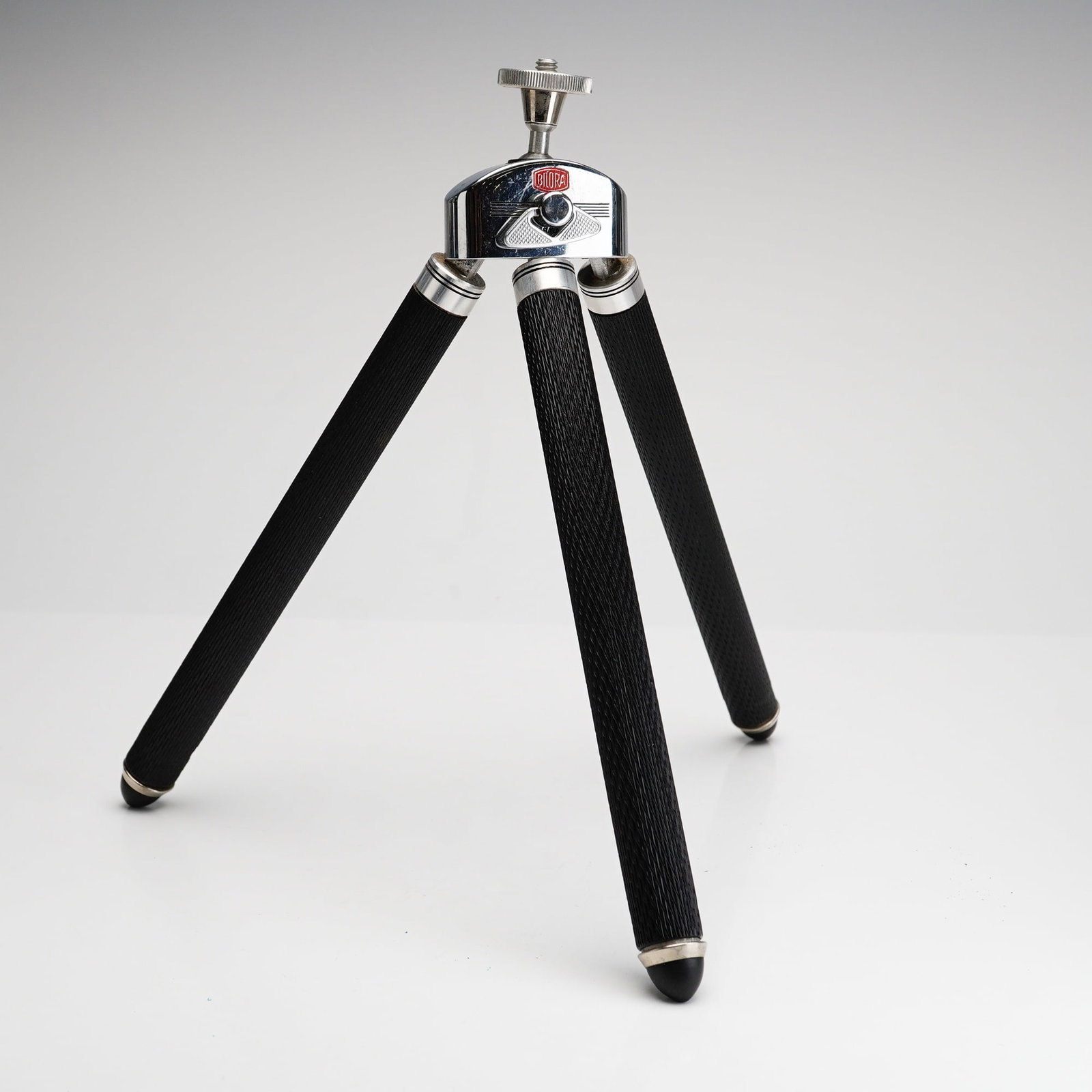 Vintage Bilora Biloret 1017 Tabletop Tripod with Leather Case: This is a German-manufactured Bilora Biloret 1017 tabletop or pocket camera tripod. The device features a chrome-plated metal head and fittings. The three legs are finished with a black textured wrap 